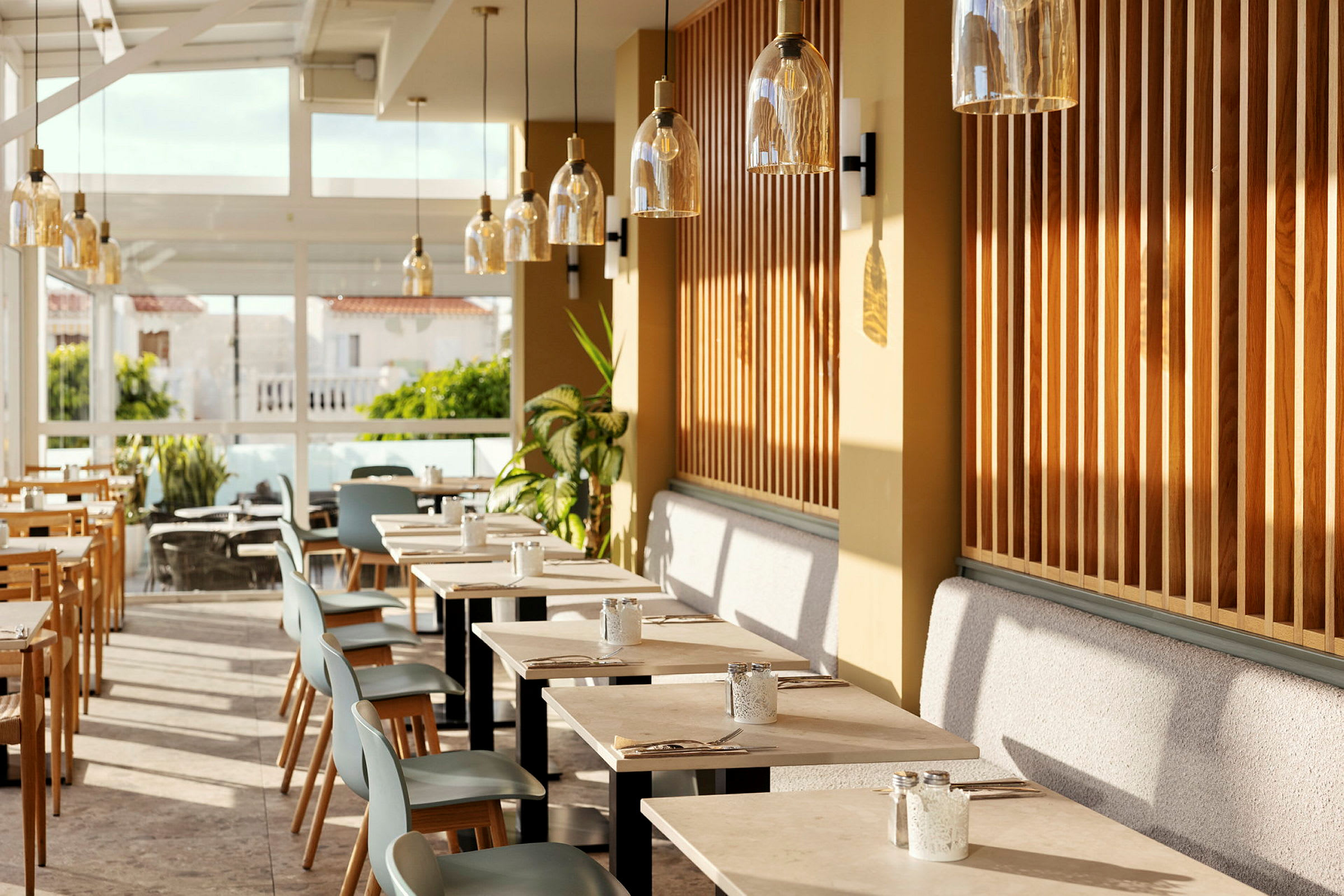 Et restaurantinteriør med moderne bord og stoler, omgitt av store vinduer og planter. (AI-generert tekst)