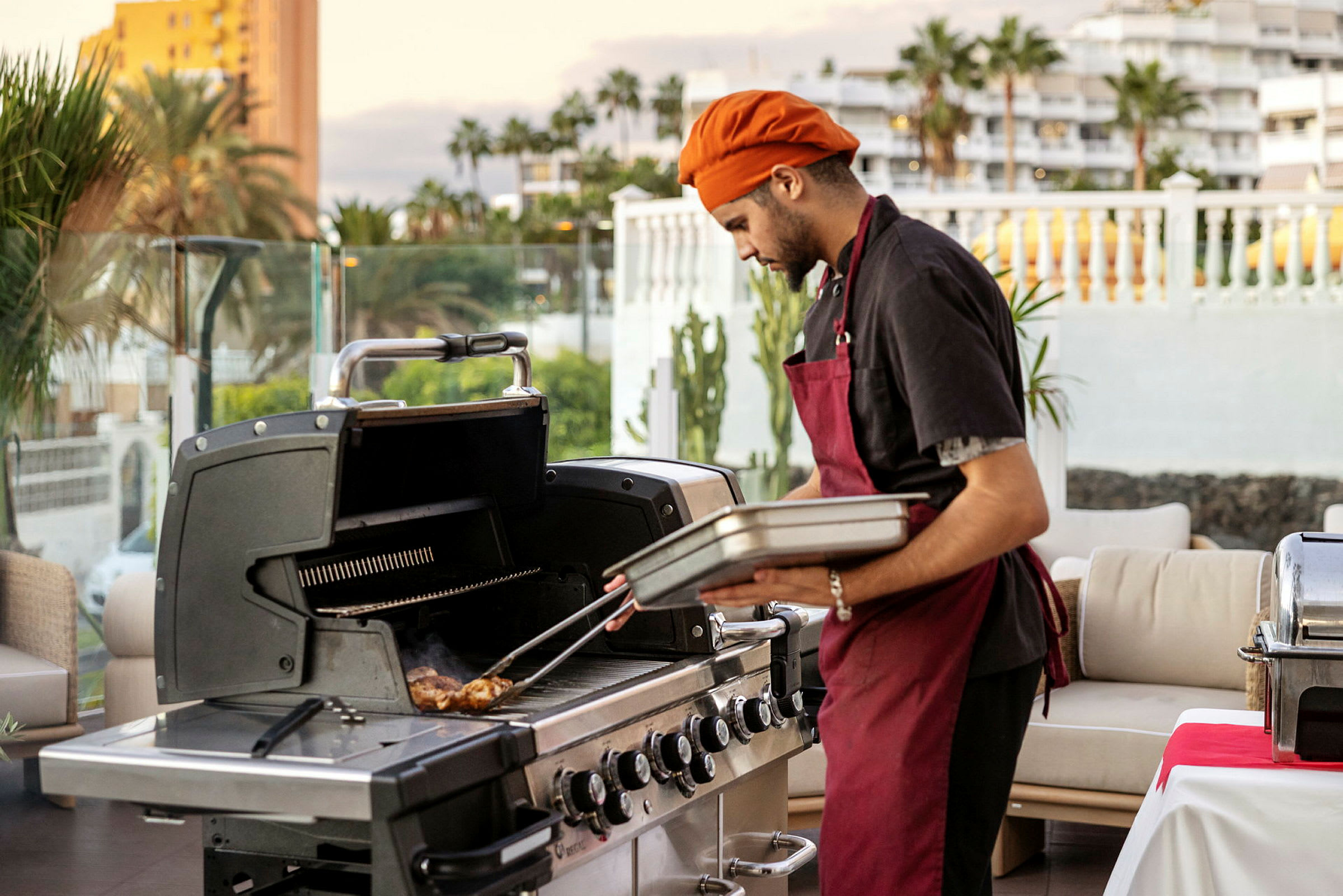 En person tilbereder mat ved en grill på en uteterrasse. (AI-generert tekst)