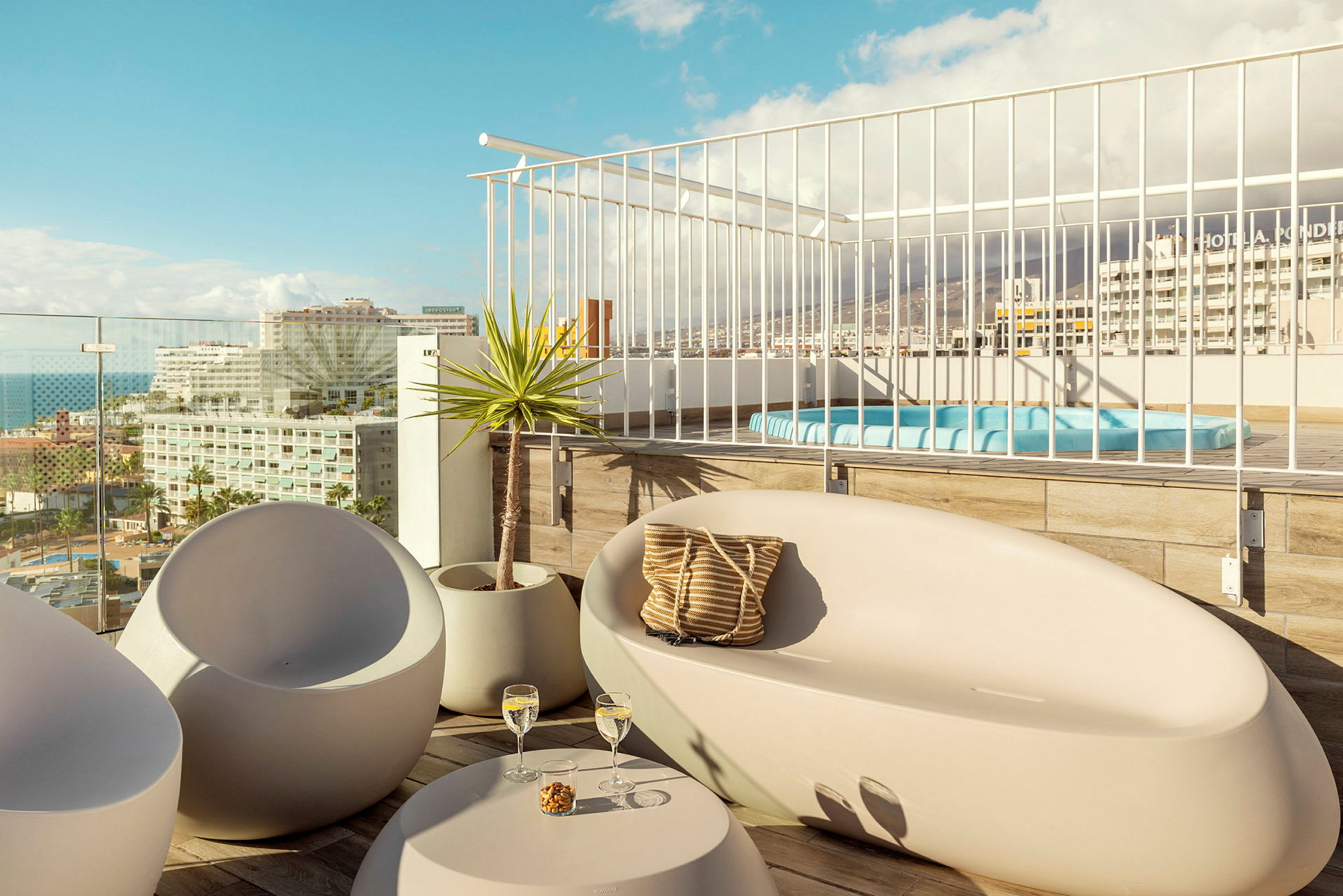 Utsikt over en møblert terrasse med sitteplasser og boblebad, samt byen i bakgrunnen. (AI-generert tekst)