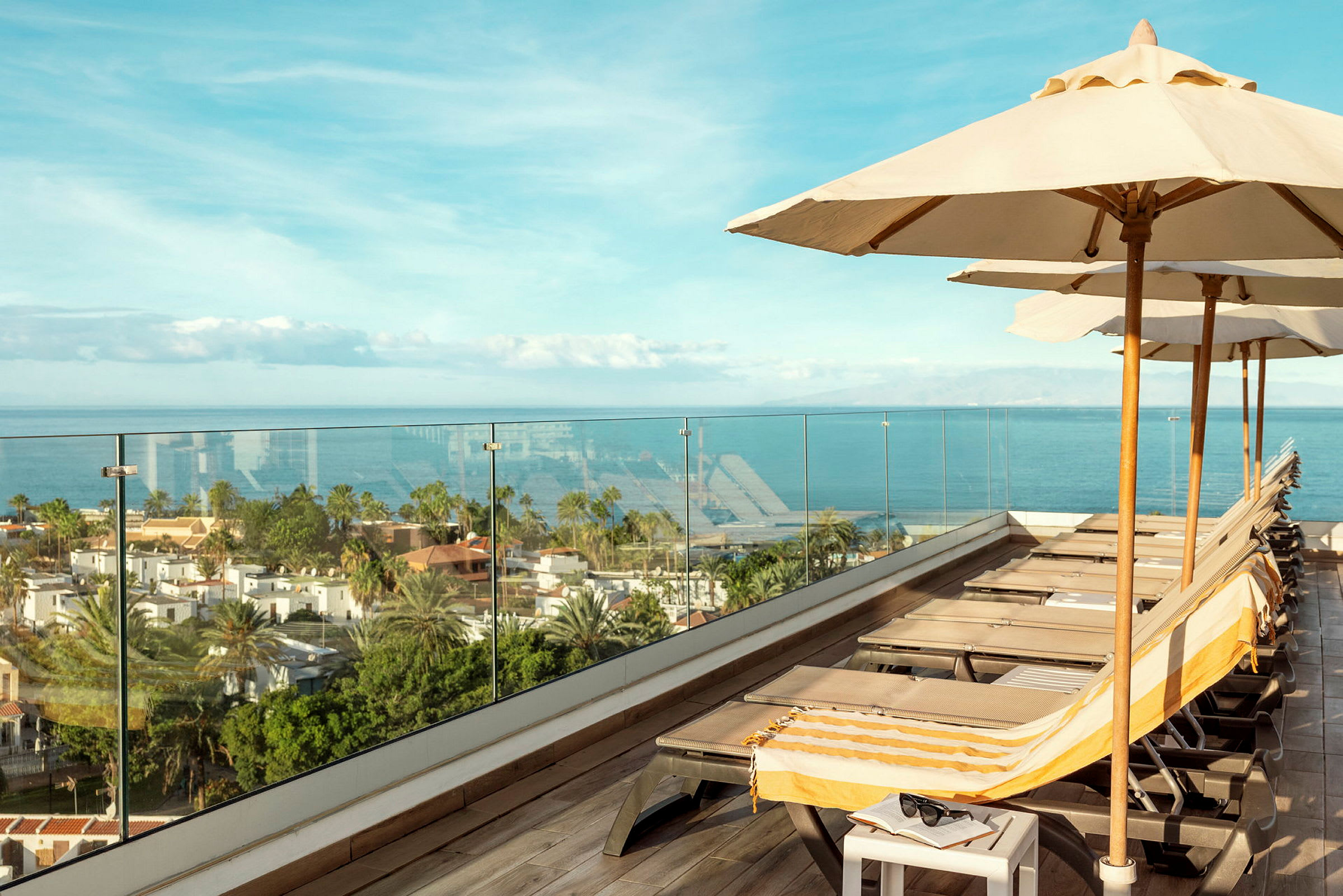 Solstoler og parasoller på en takterrasse med utsikt over havet. (AI-generert tekst)