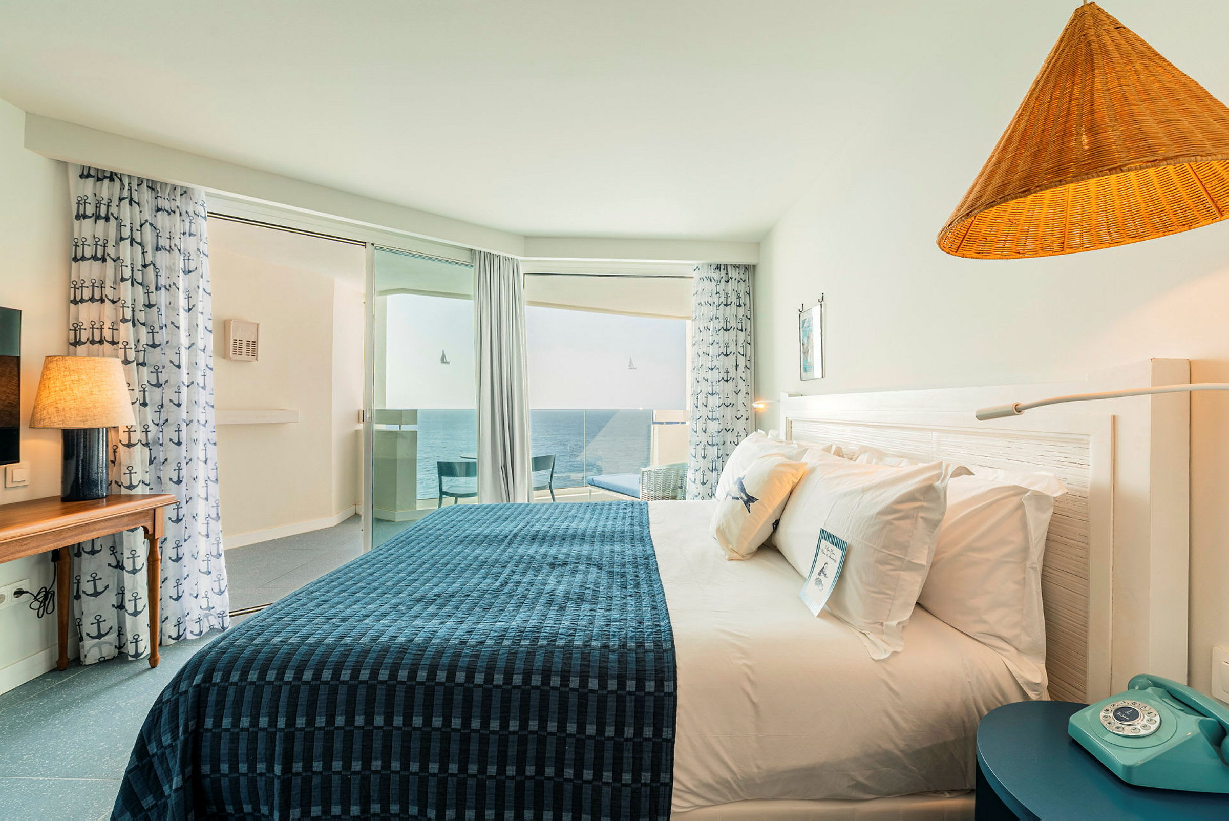 Et hotellrom med en dobbeltseng, dekorasjoner i maritimt tema og et vindu med utsikt over havet. (AI-generert tekst)