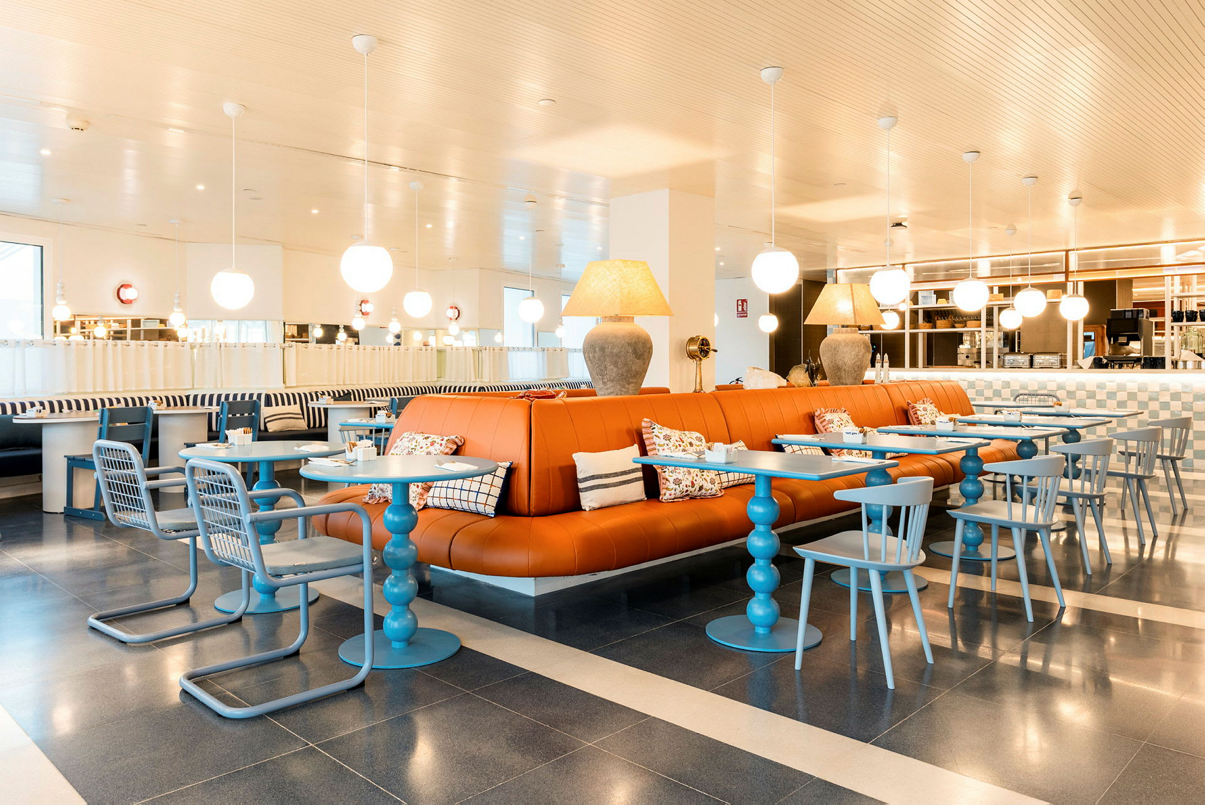 Et moderne innredet kafé med oransje skinnsofaer, blå bord og stoler samt dekorative lamper i taket. (AI-generert tekst)