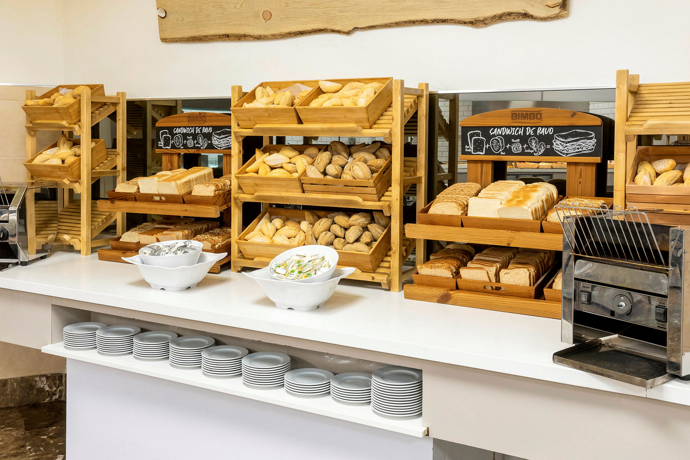 En frokostbuffet med forskjellige typer brød, skåret og uskåret, i trestativer og en brødrister. (AI-generert tekst)