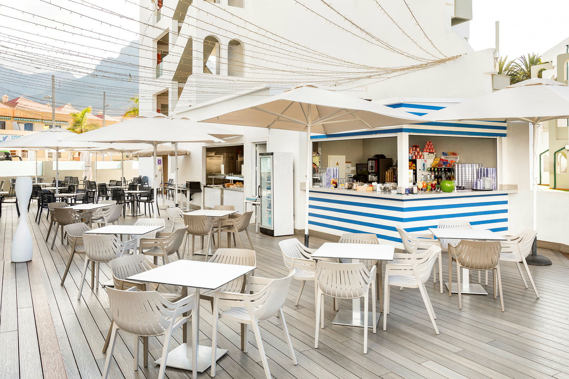 En åpen utendørs serveringsområde med hvite parasoller og en blå- og hvitstripet bar. (AI-generert tekst)