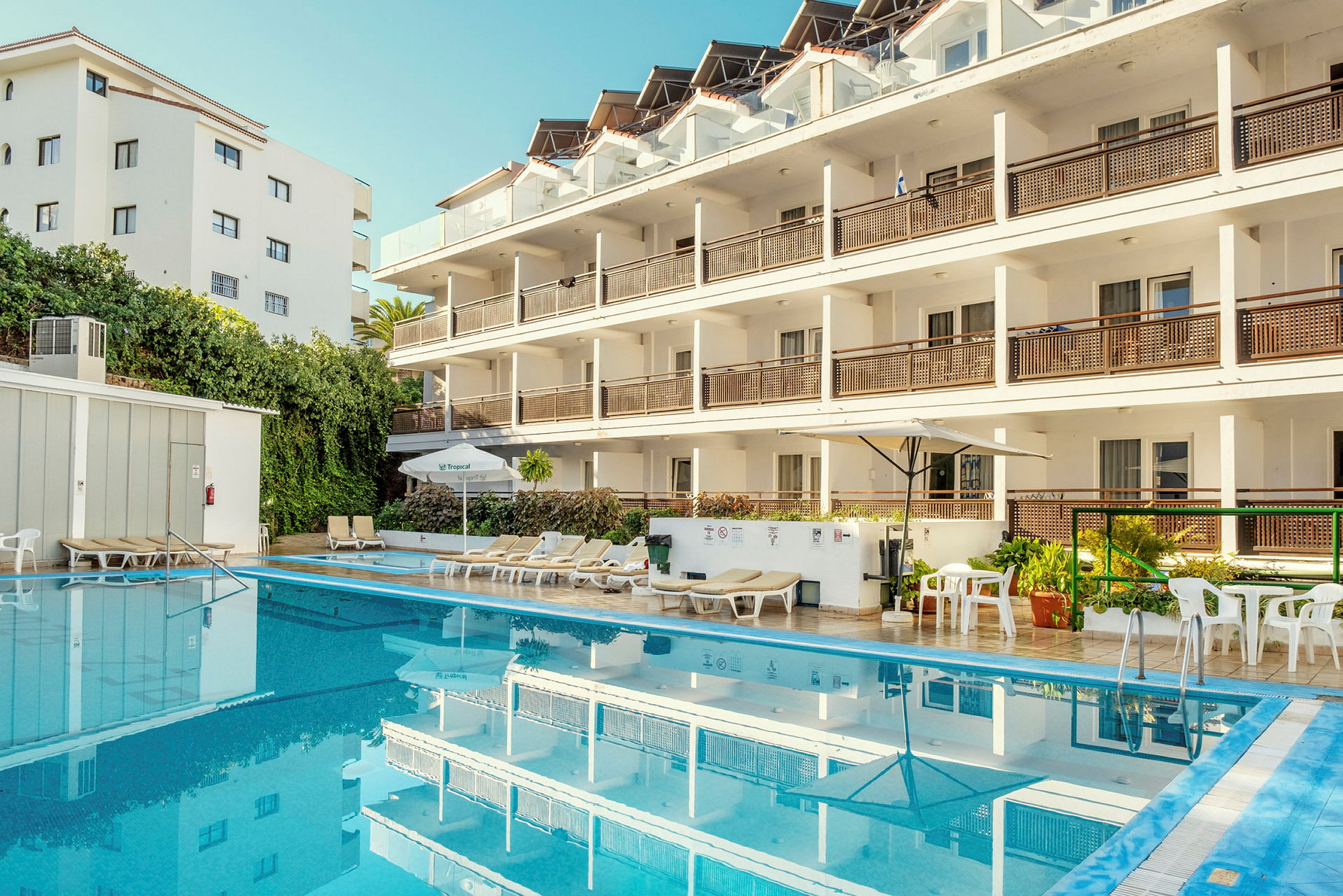En hotellbygning med flere etasjer, ved siden av et utendørsbasseng og solsenger. (AI-generert tekst)