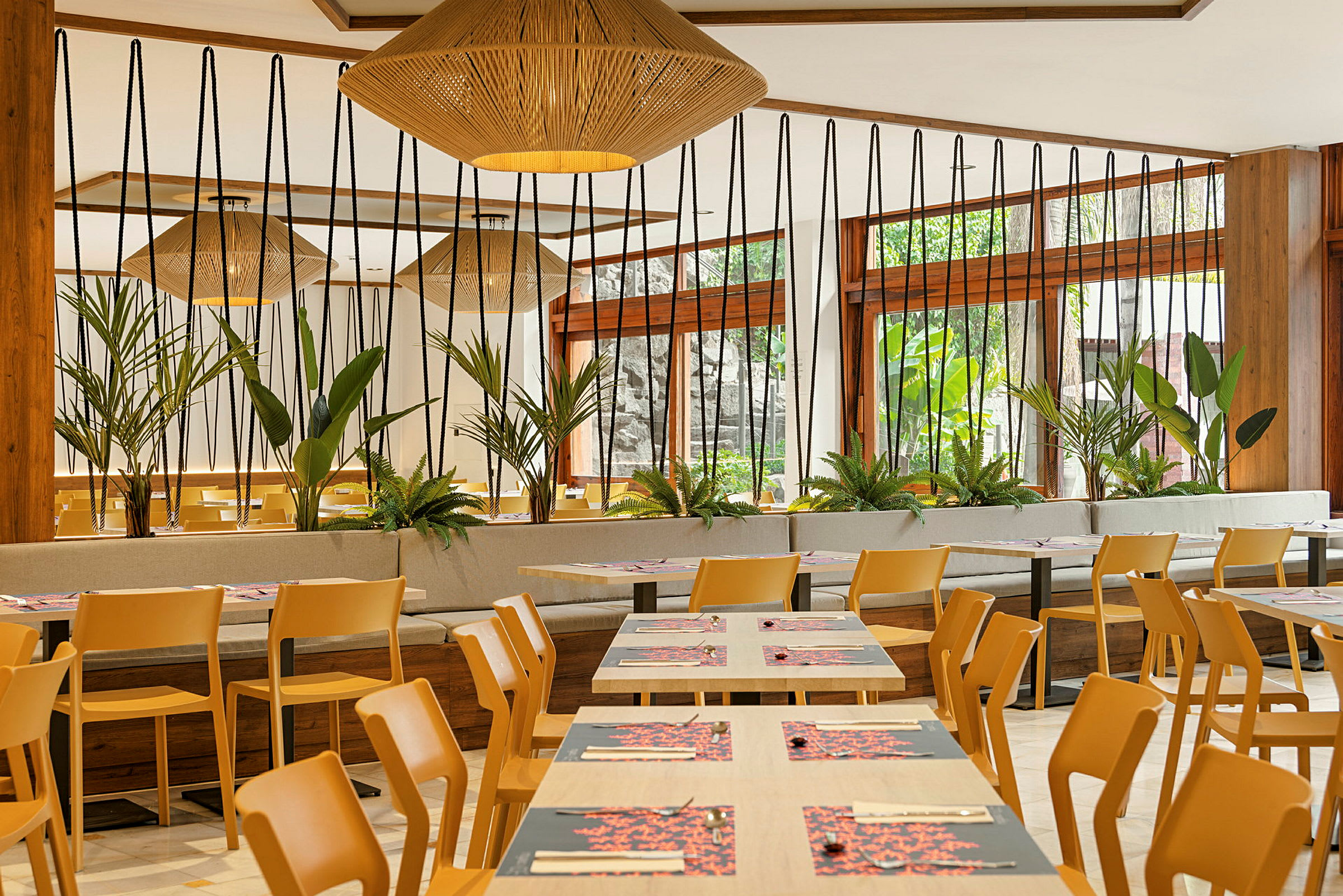 Et moderne innredet restaurantområde med trestoler, bord og grønne planter. (AI-generert tekst)