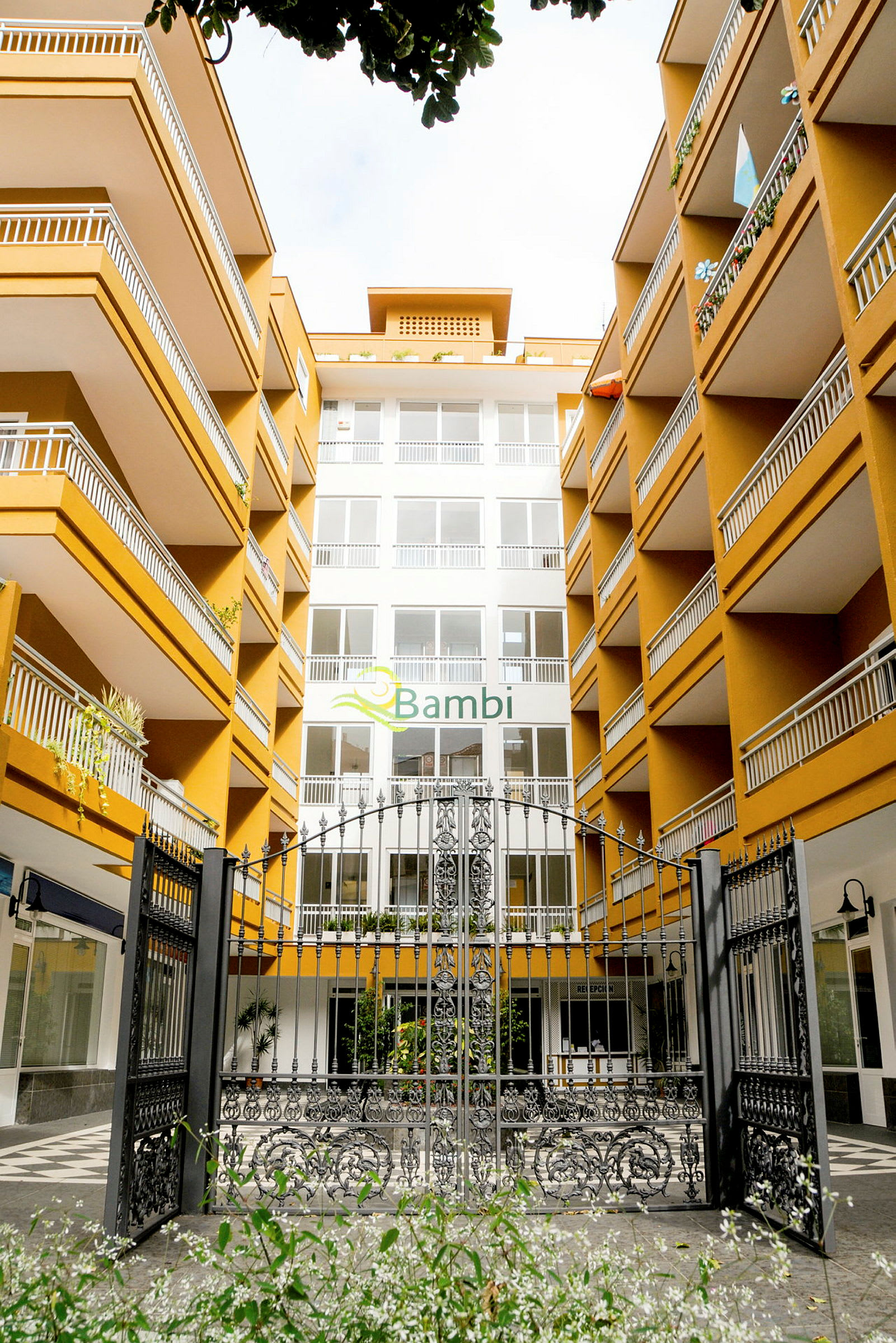 Inngang til hotellkompleks med flere etasjer og balkonger. (AI-generert tekst)