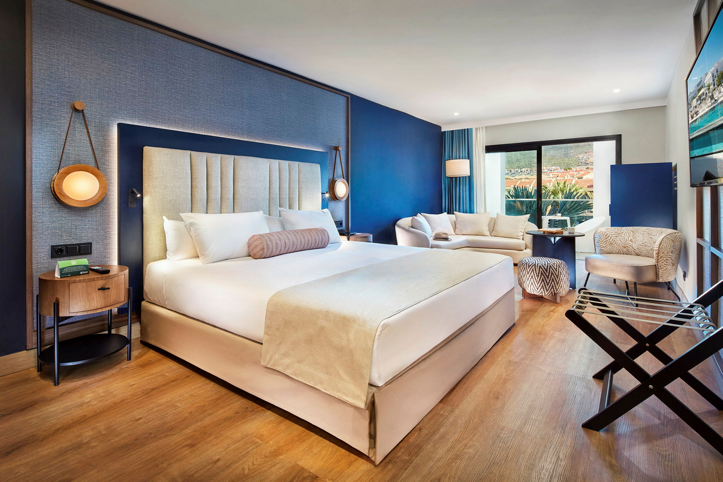 Et moderne hotellrom med en stor dobbeltseng, sittegruppe og balkong. (AI-generert tekst)