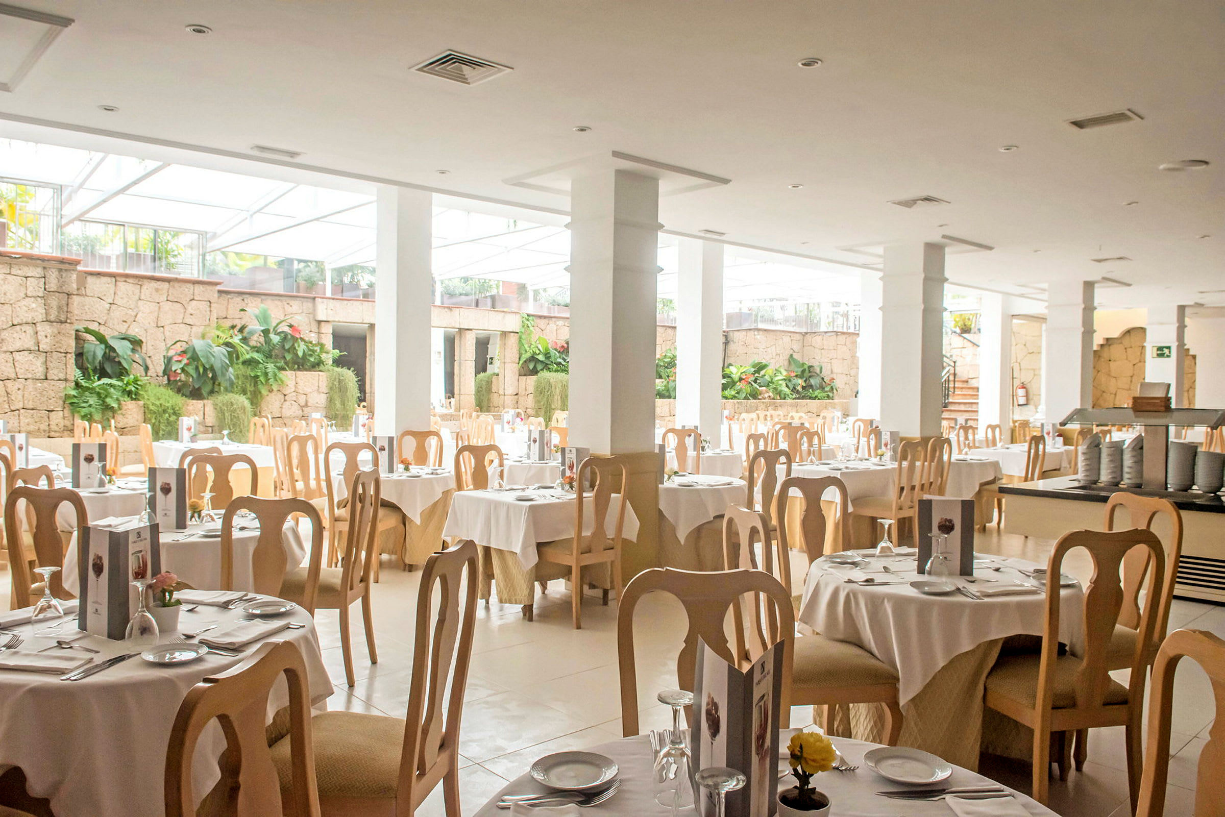 Lys restaurant med dekkede bord og trestoler. (AI-generert tekst)