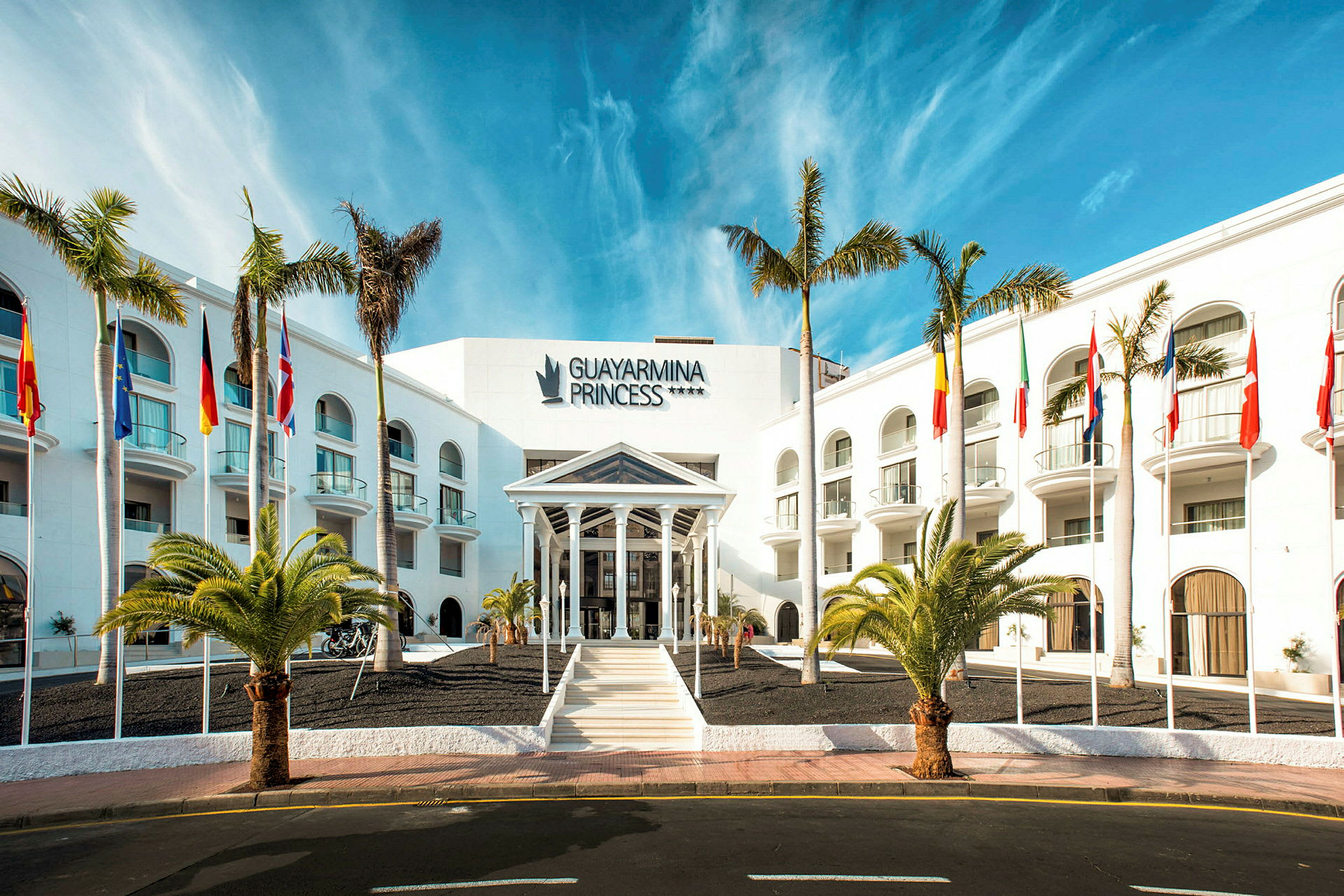 Hotell Guayarmina Princess med palmer og flagg ved inngangen. (AI-generert tekst)