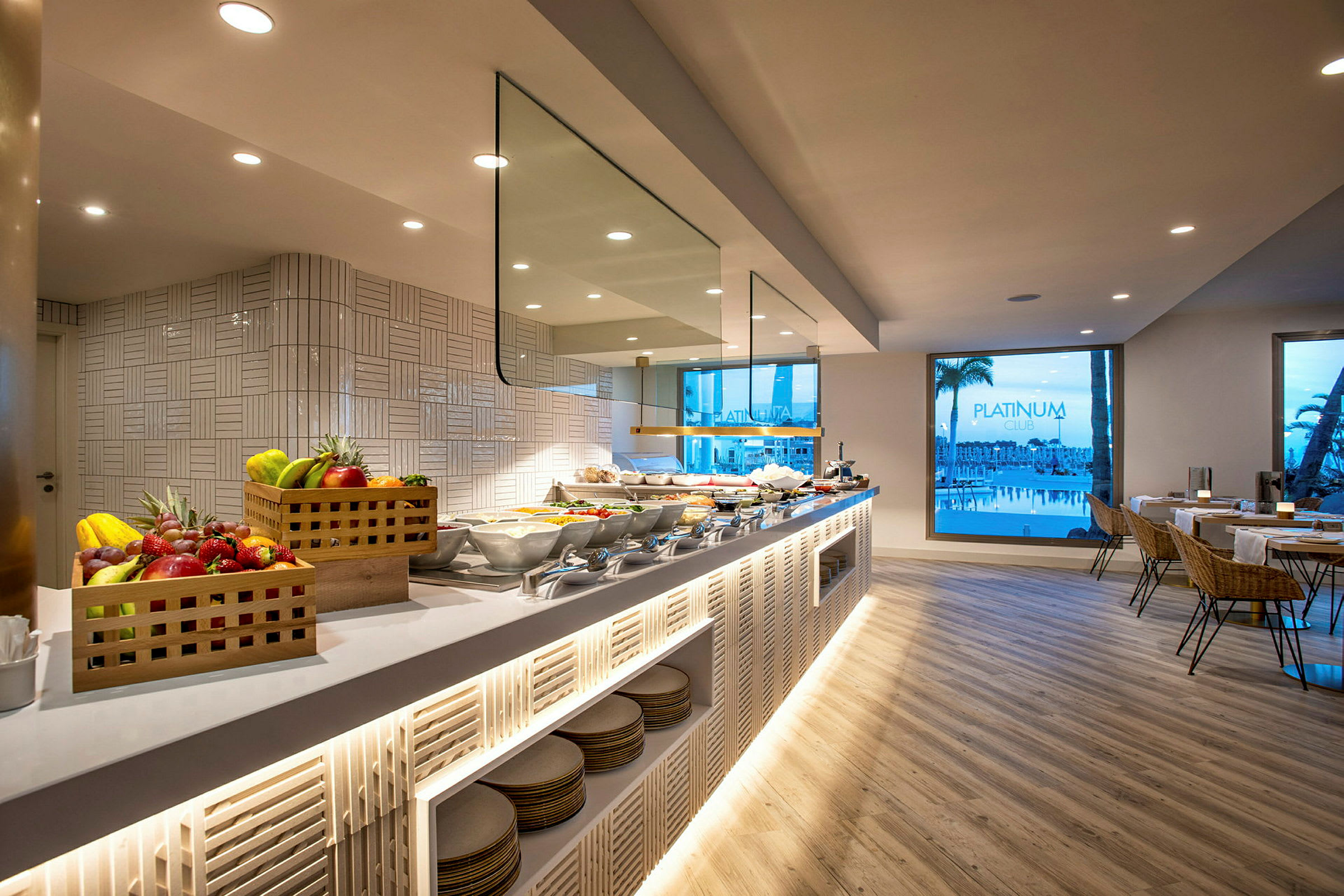 Bilde av en hotellbuffet med fruktkurver, matoppsetninger og sitteområder nær store glassvinduer. (AI-generert tekst)