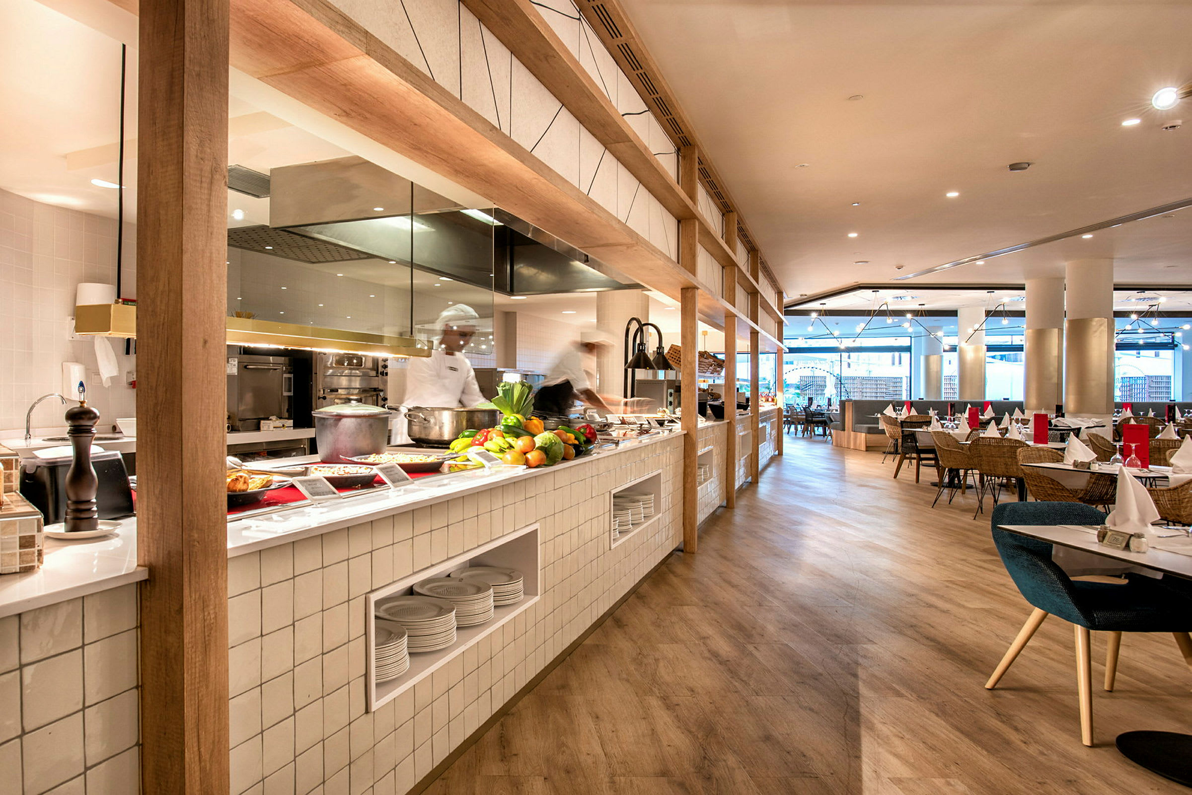 Bilde av en moderne restaurant med åpent kjøkken, benk med ferske råvarer og matservering og sitteplasser bak. (AI-generert tekst)
