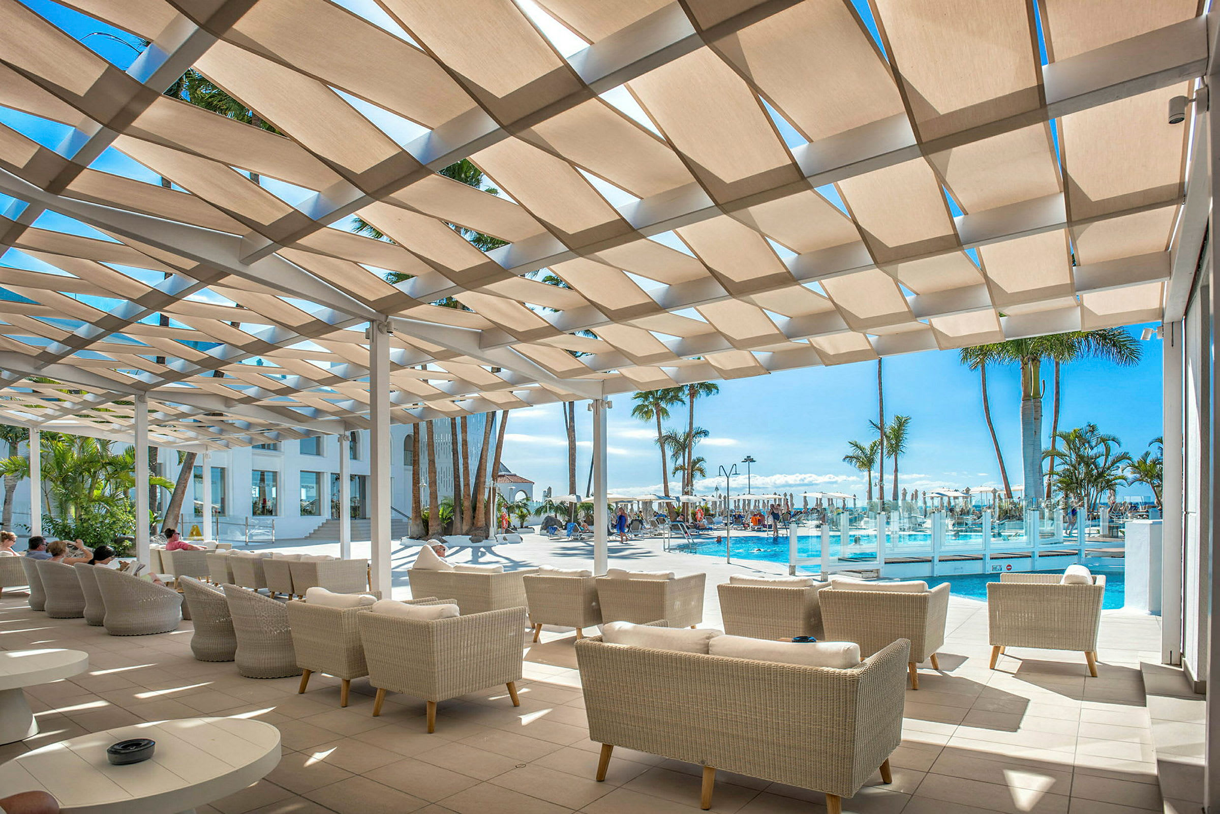 Loungeområde med sofaer under en skyggefull pergola ved et basseng. (AI-generert tekst)