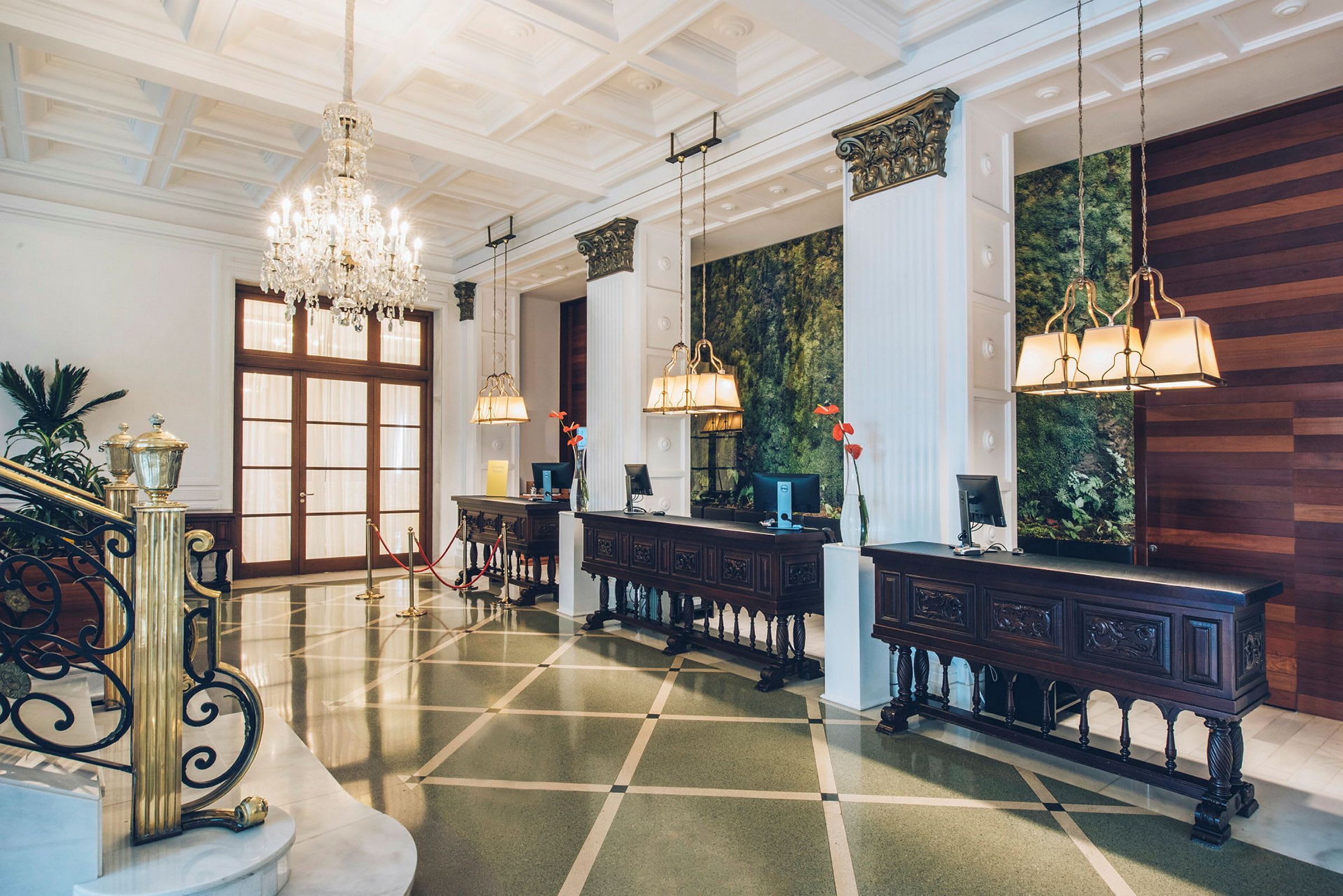 Hotellresepsjon med elegante møbler, lysekroner og et grønt dekorert område i bakgrunnen. (AI-generert tekst)