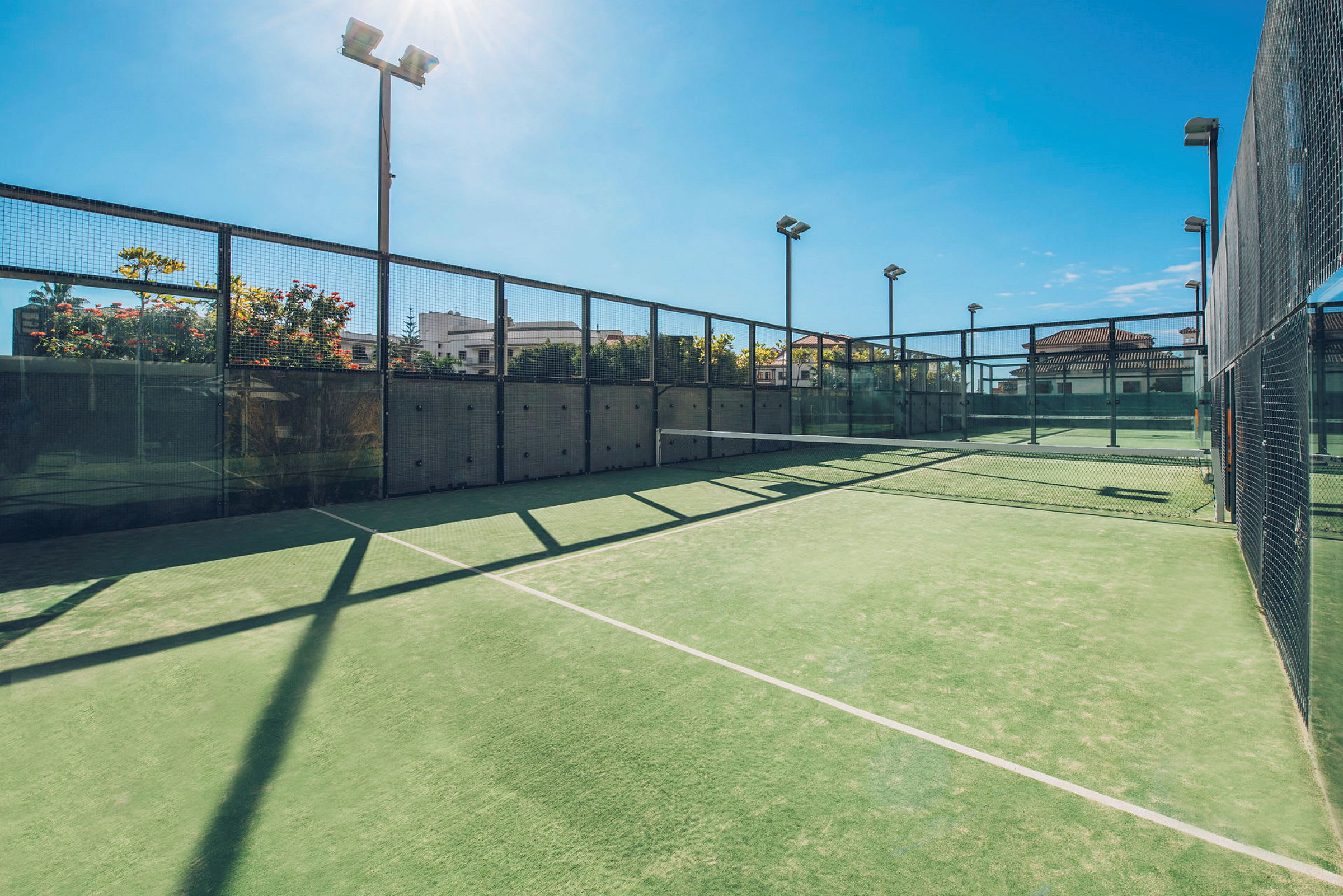 En utendørs padelbane med grønt underlag og omgitt av glass og netting. (AI-generert tekst)