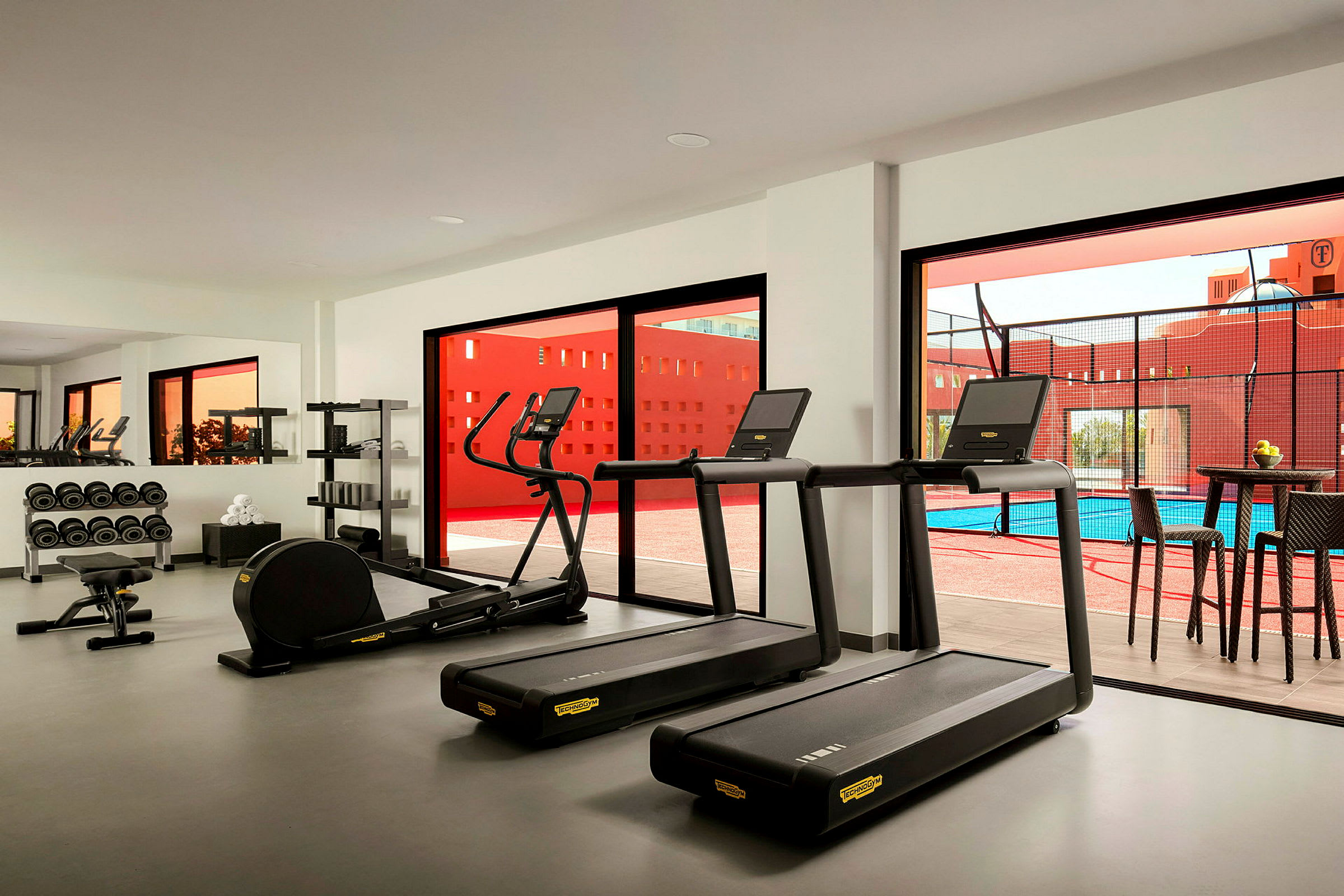 Gym med treningsmaskiner og vekter, vindu med utsikt til et basseng. (AI-generert tekst)