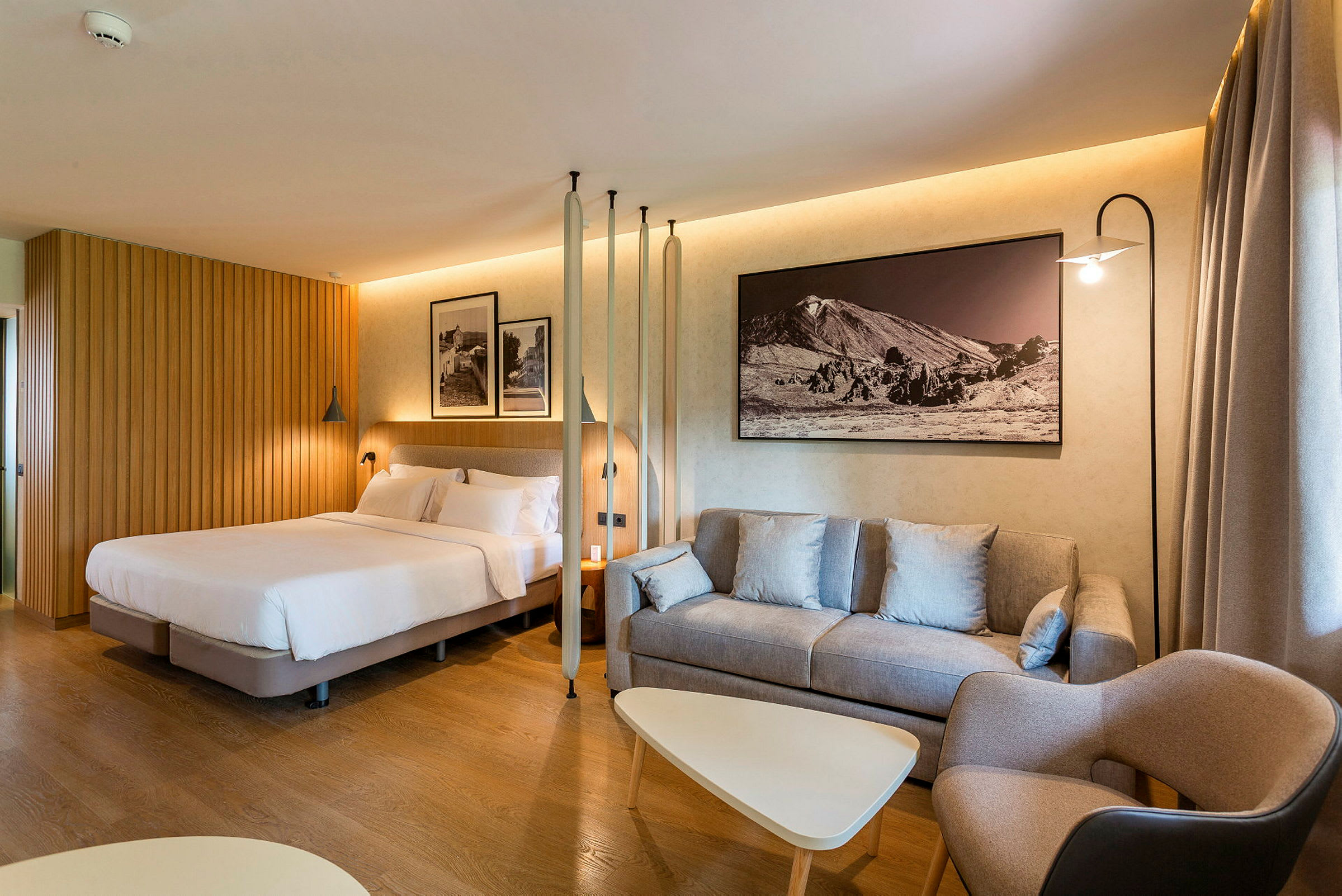 Hotellrom med seng, sofa og bord samt veggdekorasjon. (AI-generert tekst)