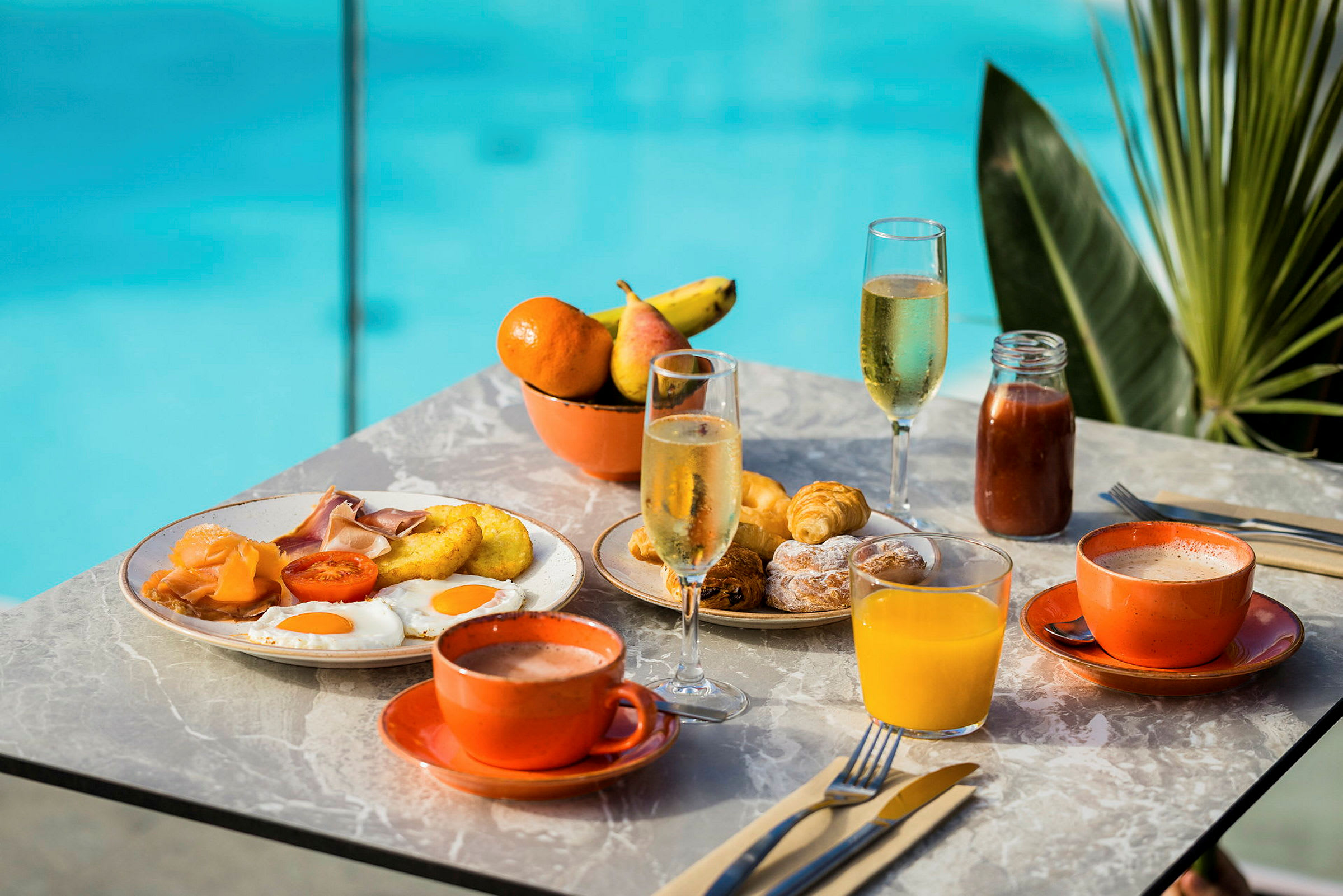 Frokostbord med forskjellige retter som egg, pølser, croissanter og drikke som juice og kaffe. Et basseng er synlig i bakgrunnen. (AI-generert tekst)