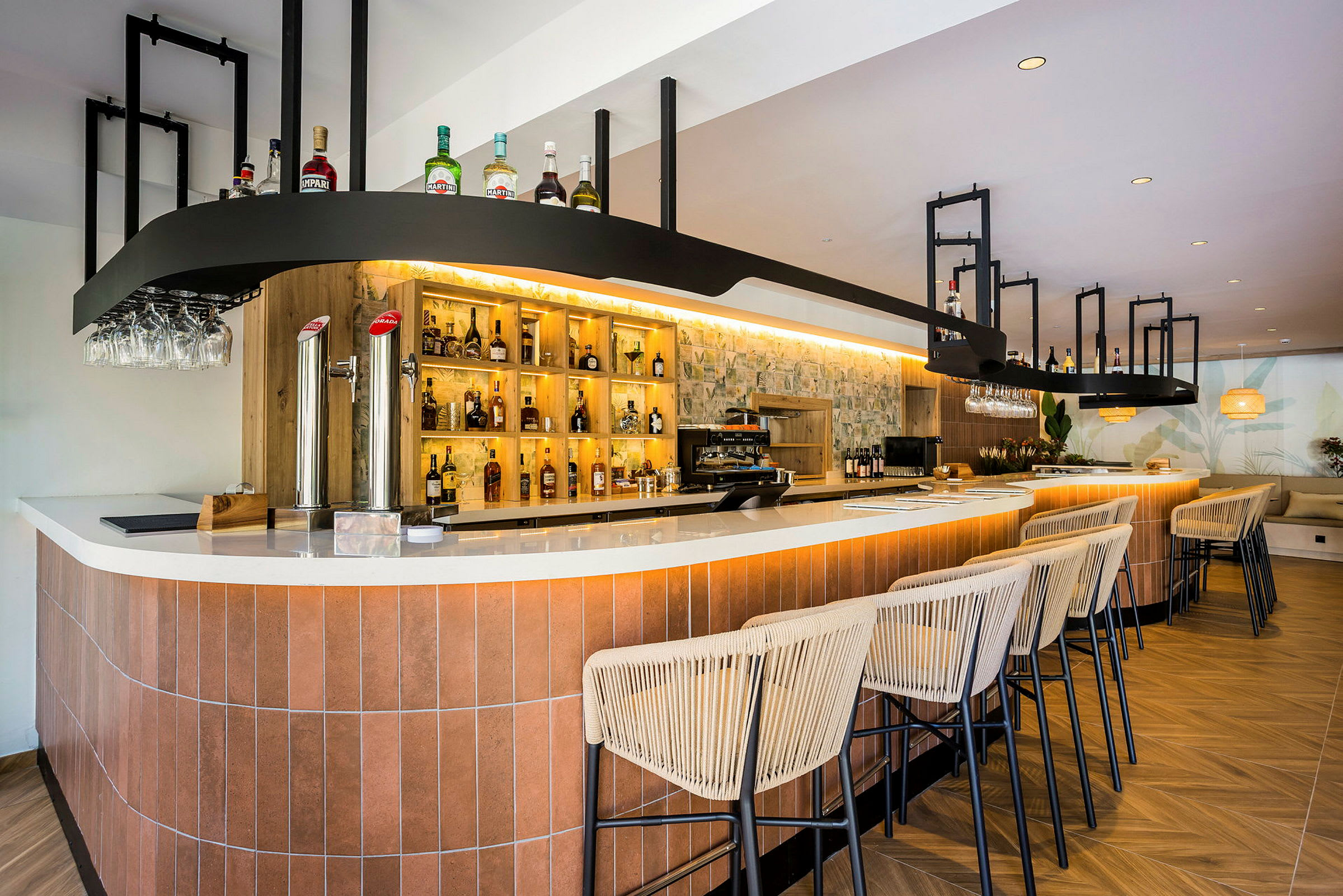 En moderne bar med en lang bardisk, opplyste hyller med flasker og komfortable barstoler i tre og lin. (AI-generert tekst)