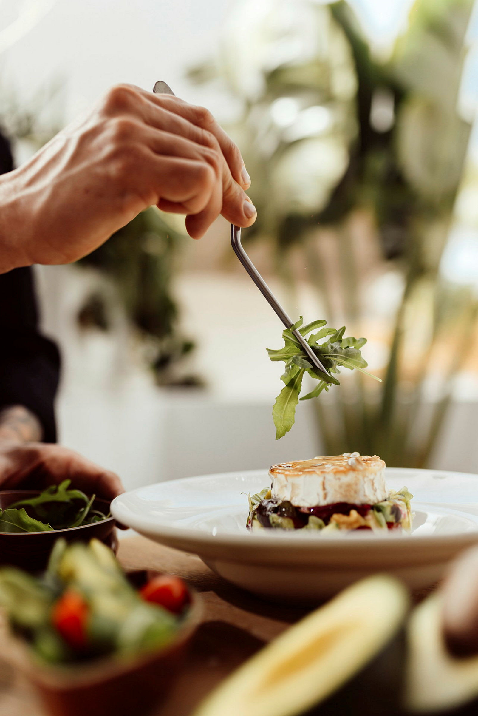 En hånd holder en gaffel med salat foran en tallerken med ost og grønnsaker. (AI-generert tekst)