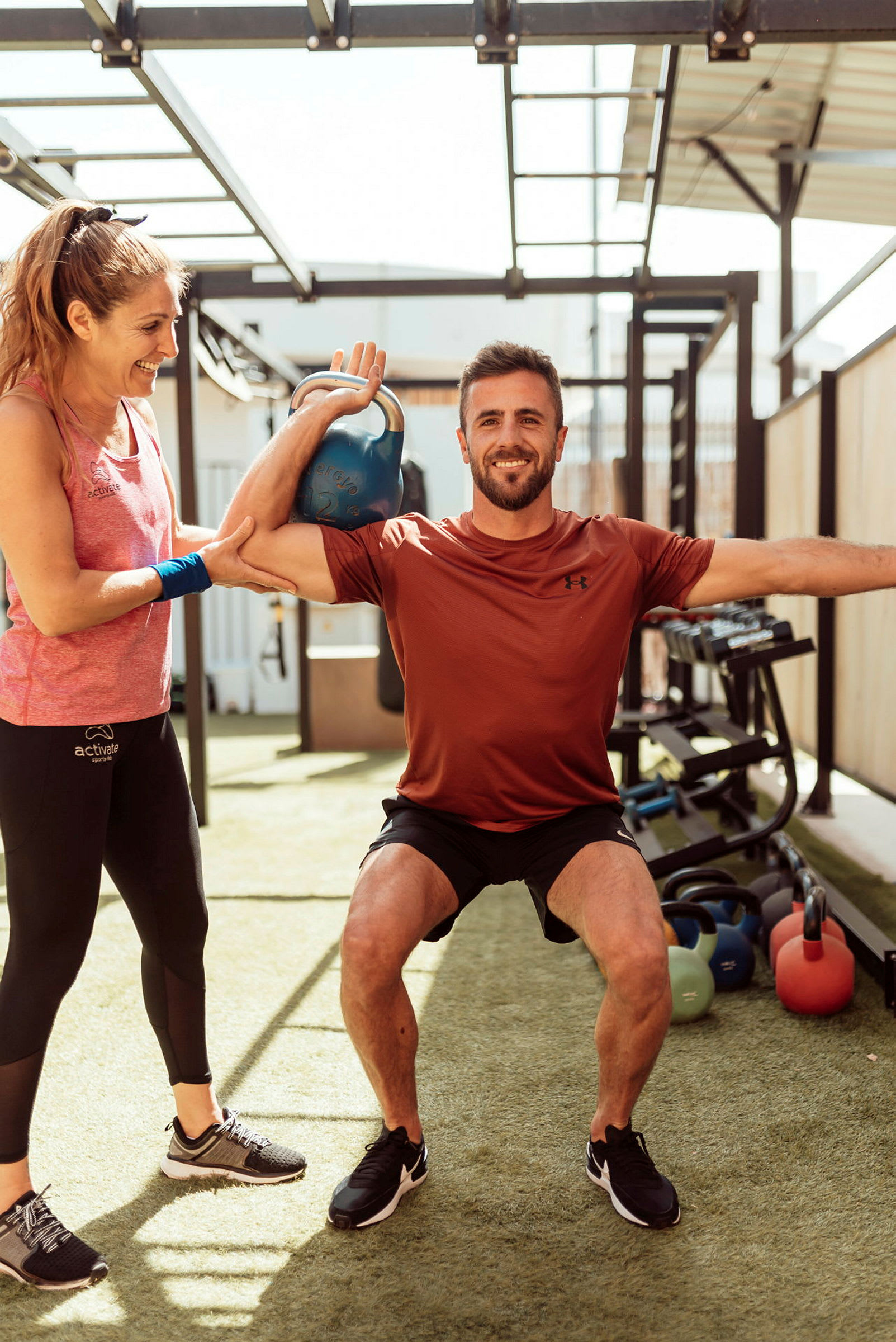 Person trener med kettlebell og får assistanse utendørs. (AI-generert tekst)