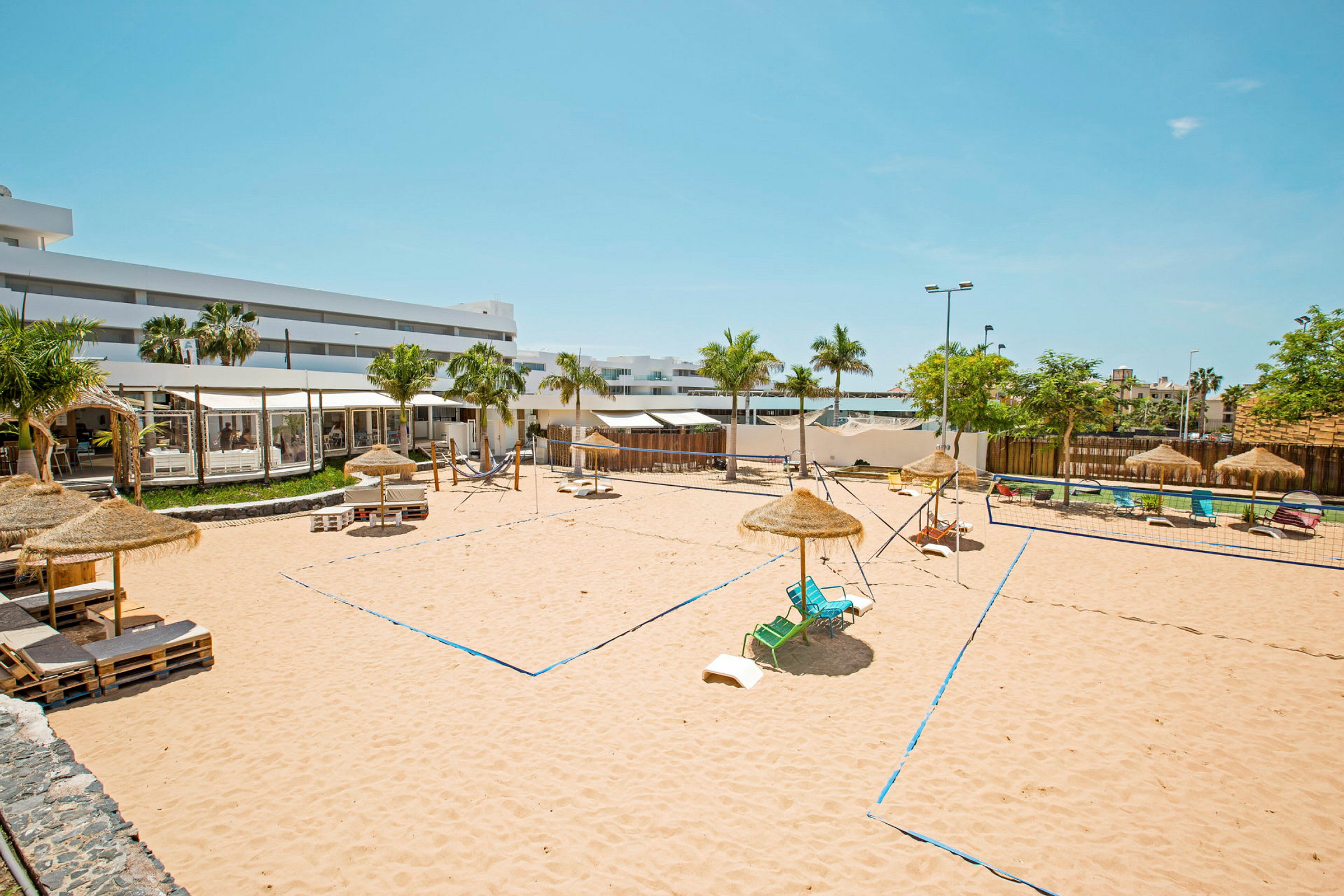 Bilde av en sandvolleyballbane med parasoller og solsenger rundt. (AI-generert tekst)