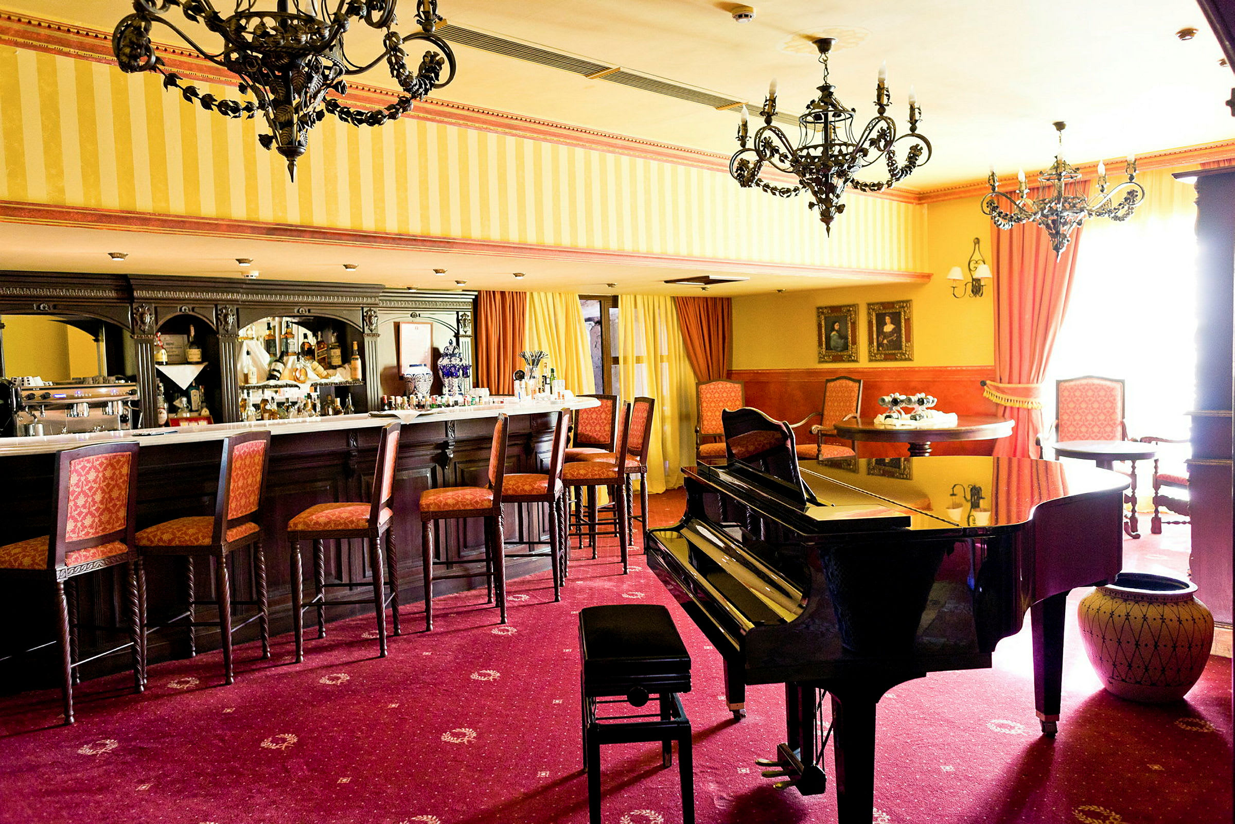 En barlounge med stoler ved bardisken, et piano i forgrunnen og elegante lysekroner i taket. (AI-generert tekst)