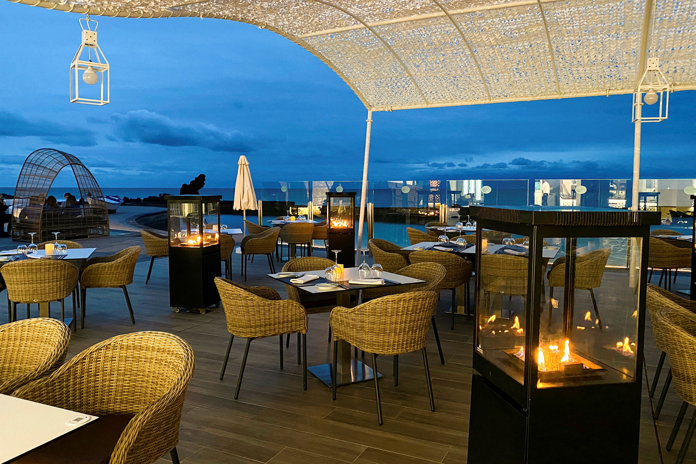 Utendørsrestaurant med bord, stoler og peiser under kveldshimmelen. (AI-generert tekst)