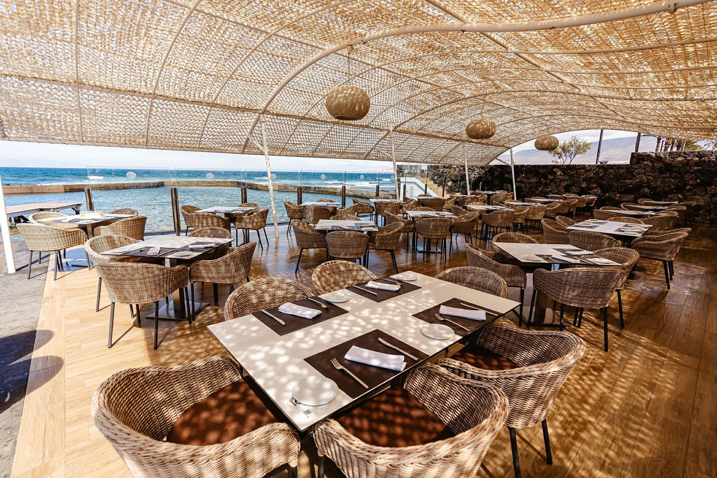 Utendørs restaurant med rottingseter og utsikt over havet. (AI-generert tekst)