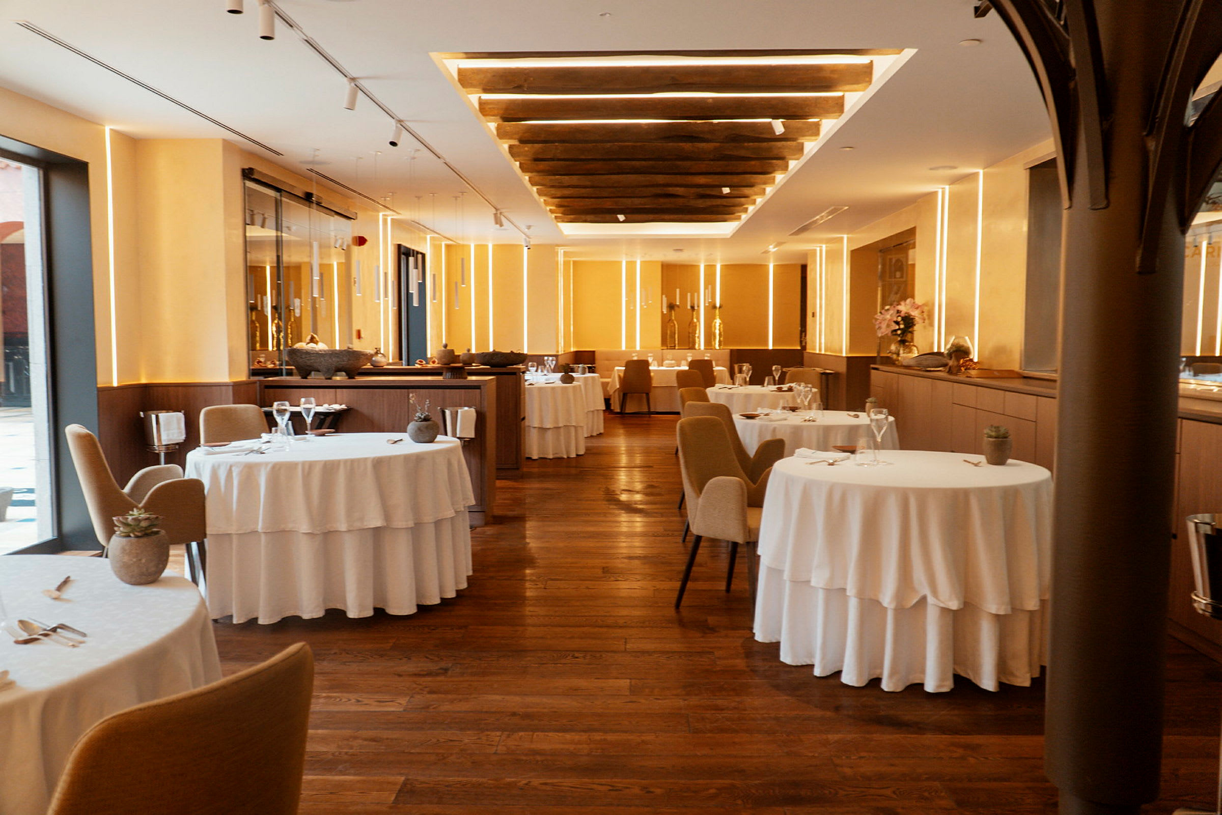 Et elegant innredet restaurantområde med hvite duker, trestoler og varm belysning. (AI-generert tekst)