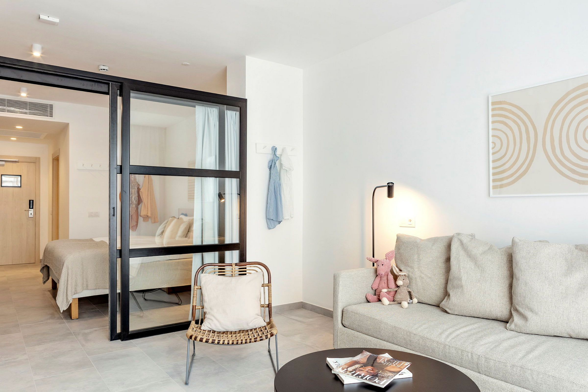 Et moderne hotellrom med soveplass og sitteområde. En glassvegg deler rommet. (AI-generert tekst)