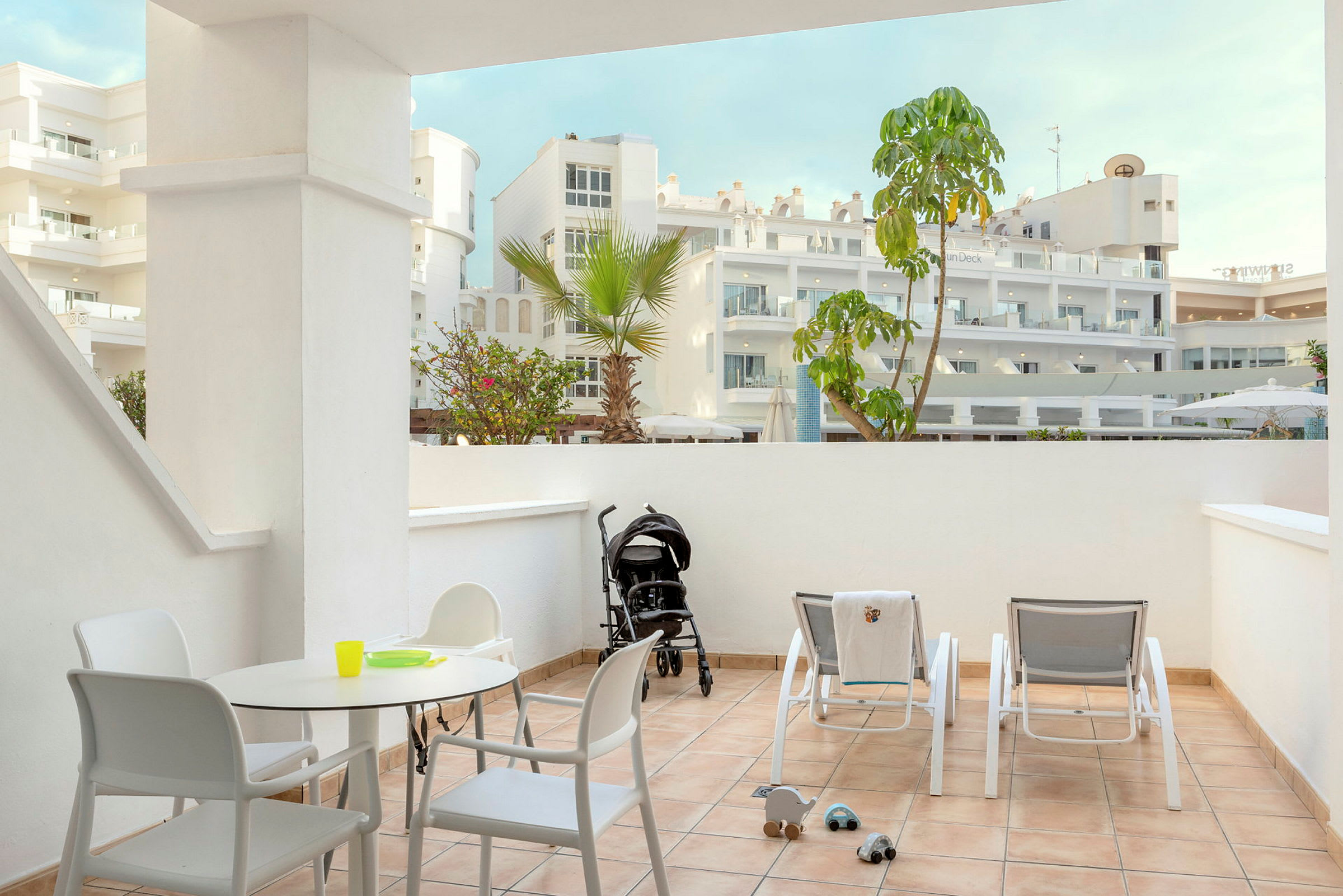 Bilde av en romslig terrasse med solstoler, bord og stoler samt en barnevogn. (AI-generert tekst)