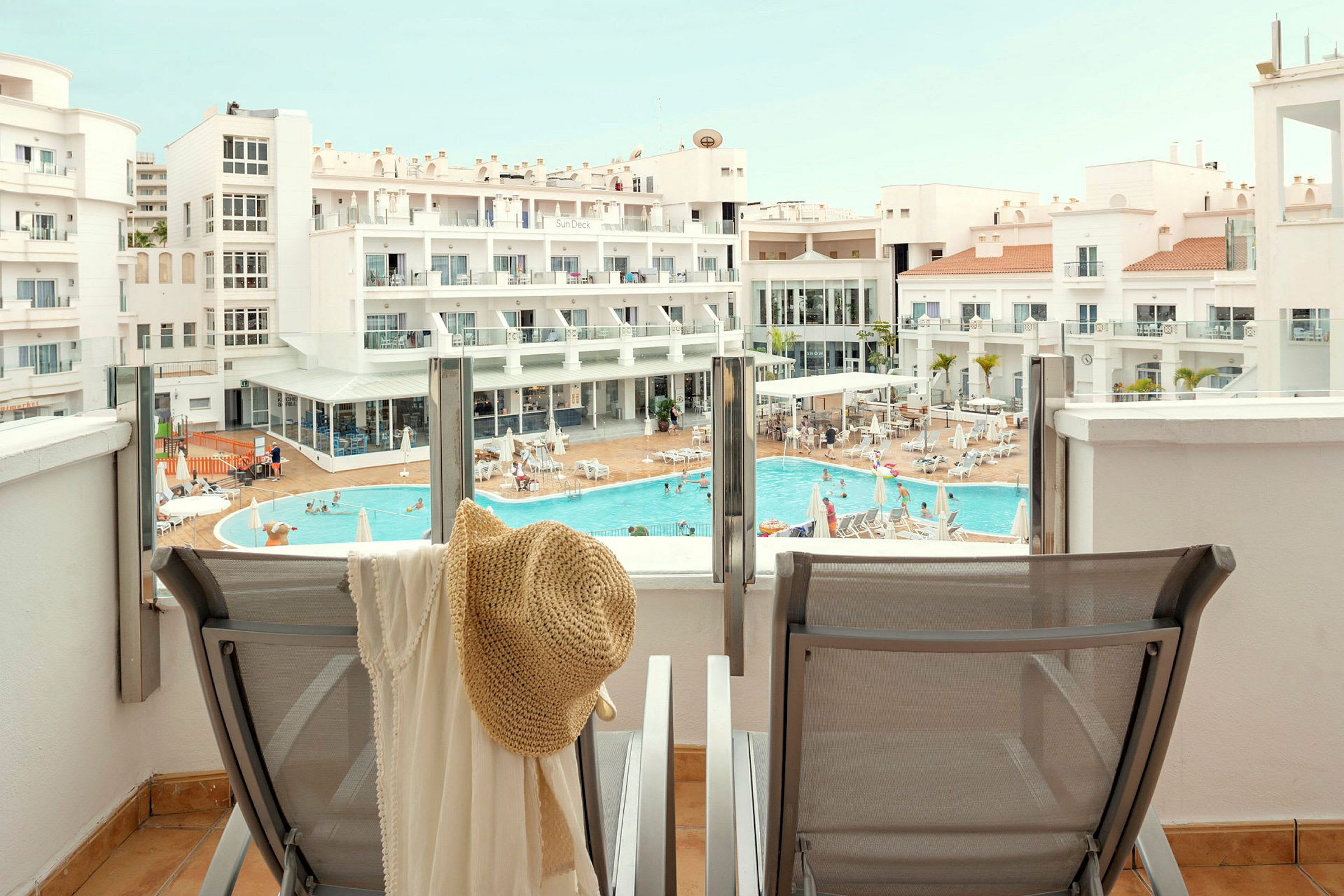 Utsikt fra en terrasse mot et basseng og hotellbygg. (AI-generert tekst)