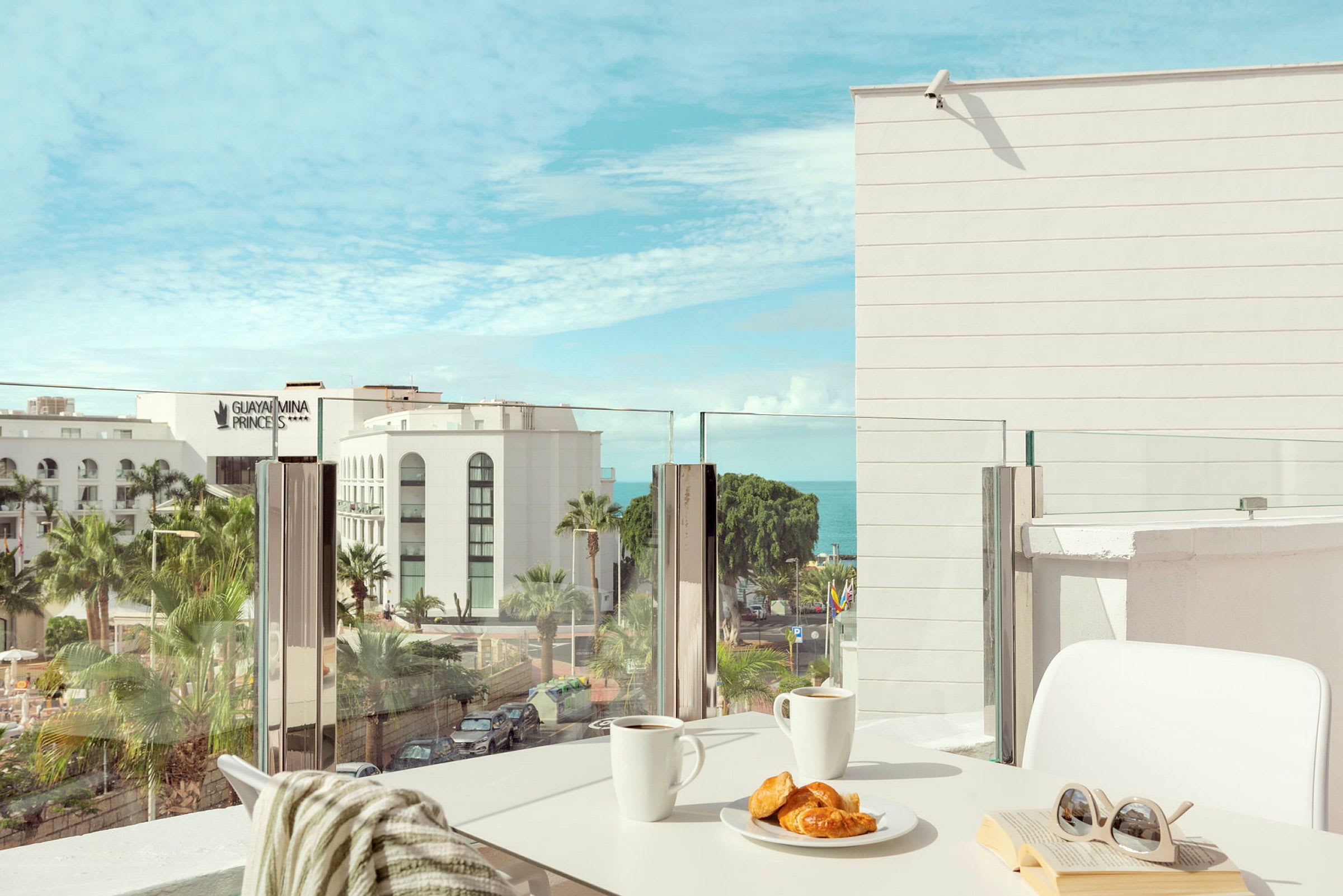 Utsikt fra en balkong med frokost på bordet og utsikt over et hotell og havet. (AI-generert tekst)