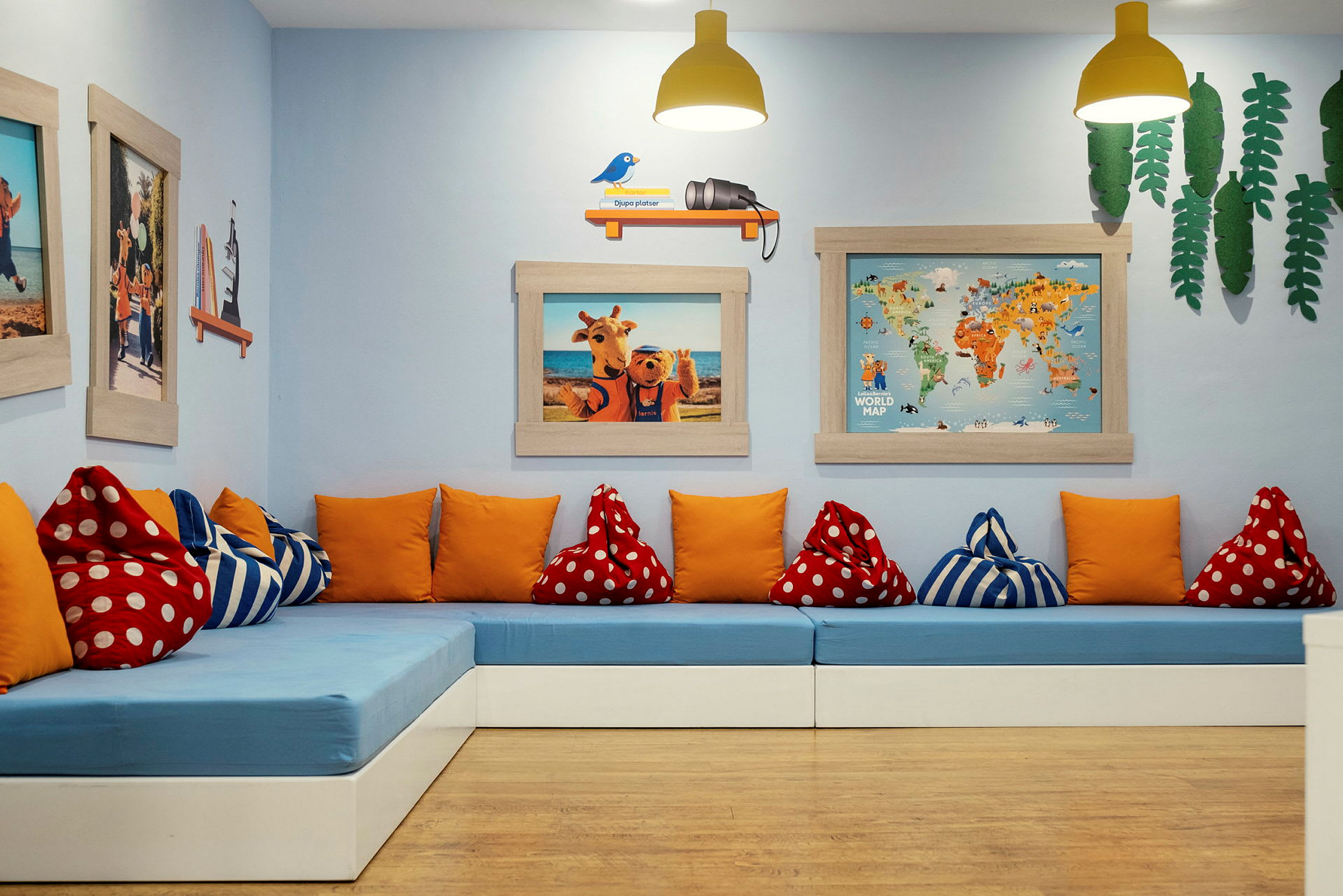 Hvilested med blå benker, oransje og mønstrede puter, og forskjellige dekorasjoner på veggen inkludert kart og fotografier. (AI-generert tekst)