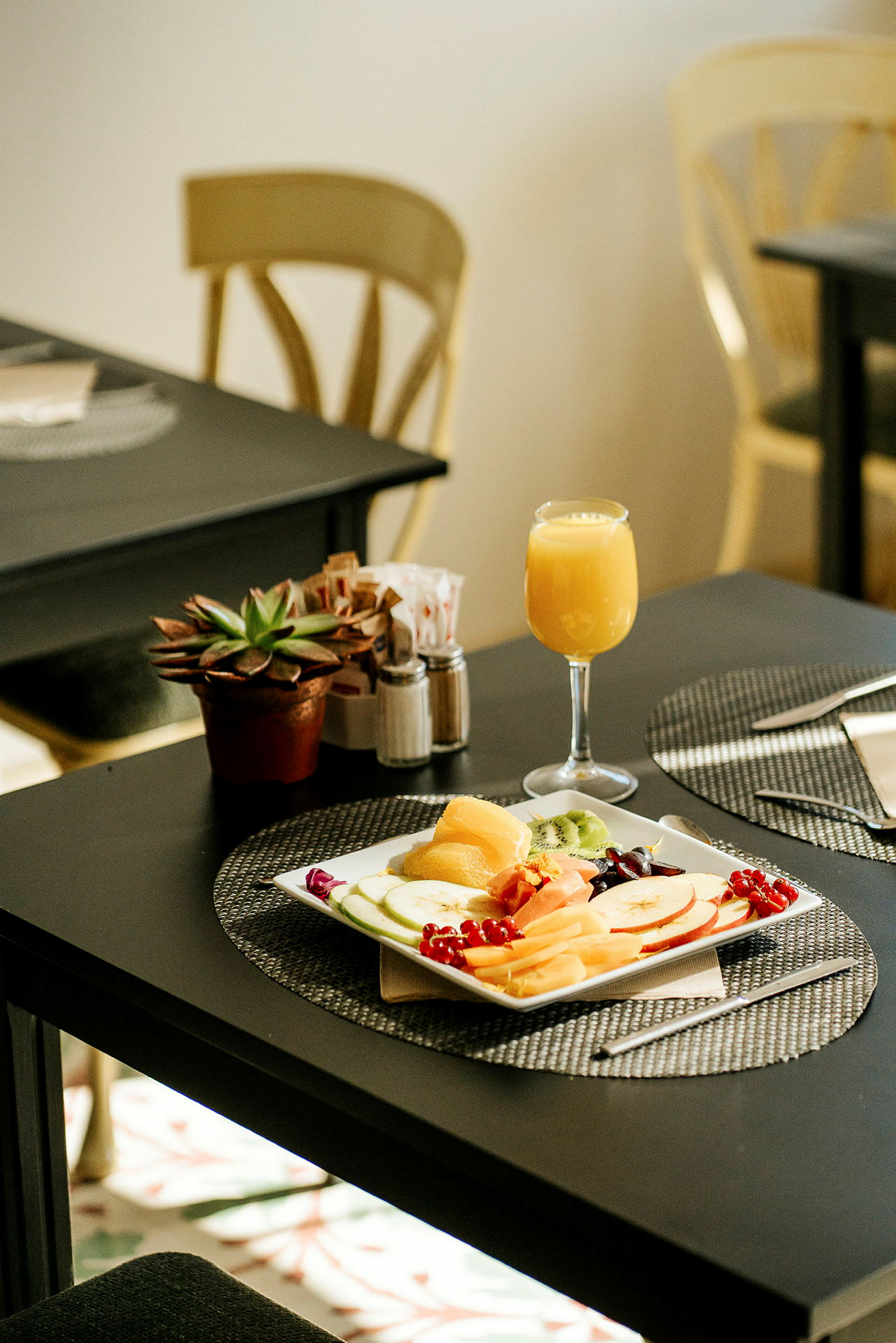 Et bord med en tallerken fylt med frukt, et glass appelsinjuice og en potteplante. (AI-generert tekst)