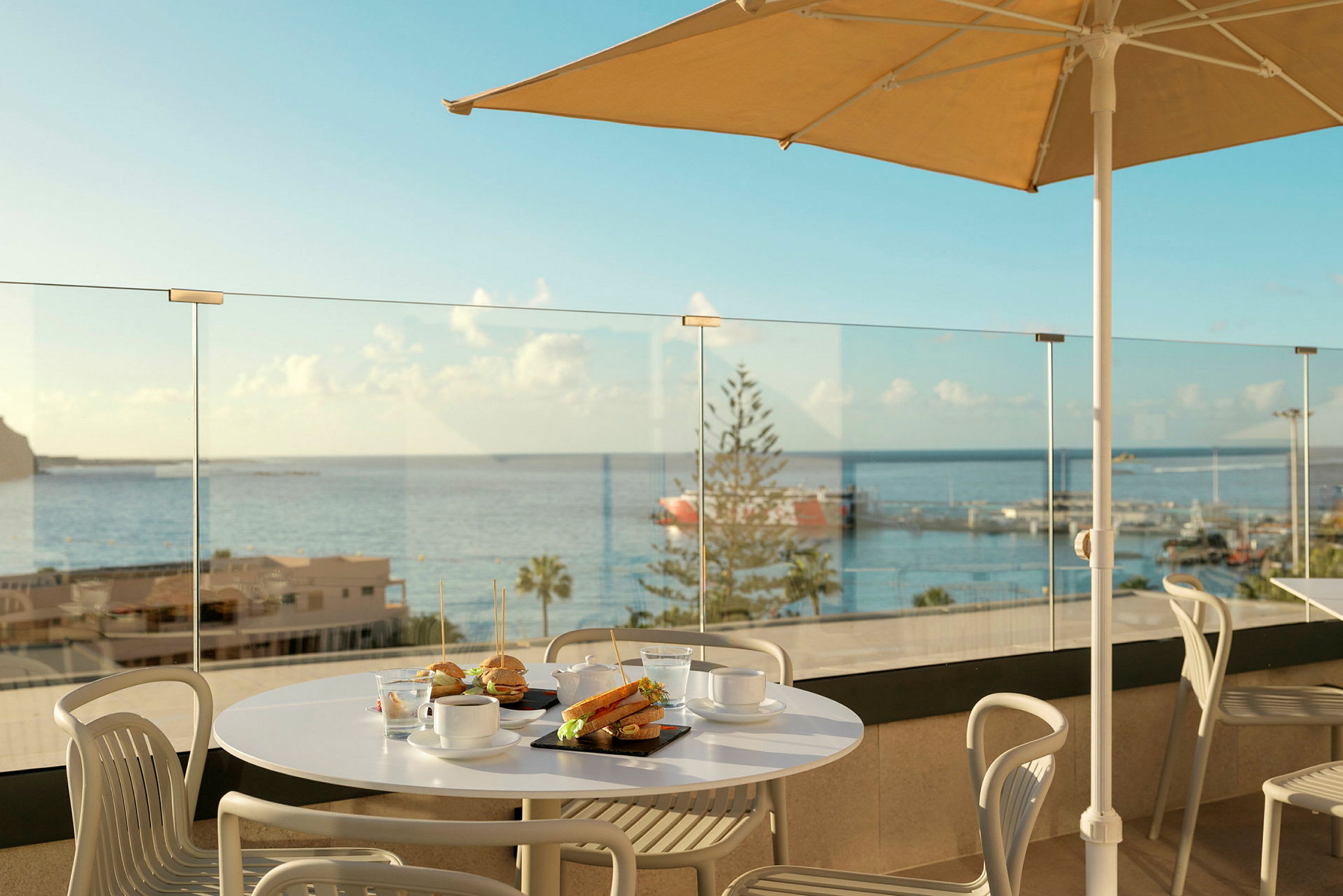 En spiseplass med bord og stoler på en terrasse med utsikt over havet. (AI-generert tekst)