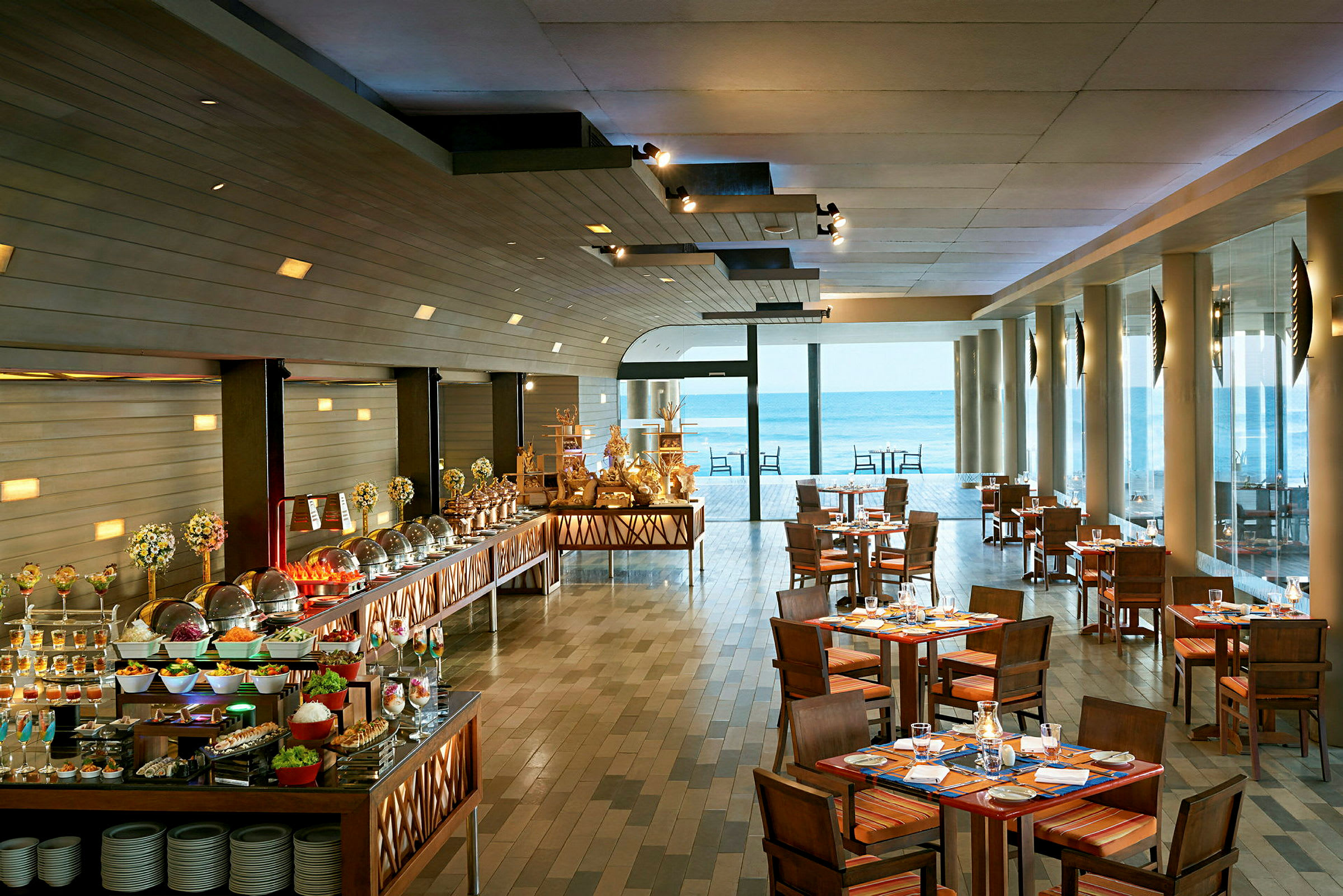 Bilde av en restaurant med dekkede bord og en buffé med ulike retter, samt store vinduer som vender ut mot havet. (AI-generert tekst)
