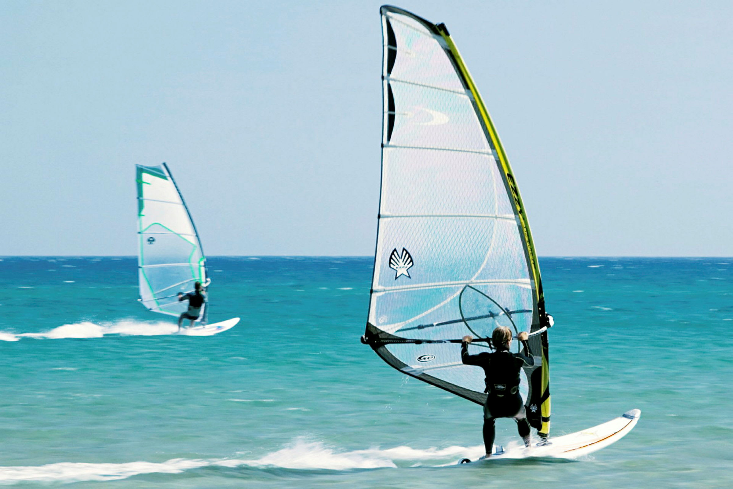 To personer windsurfer på havet under en klar himmel. (AI-generert tekst)
