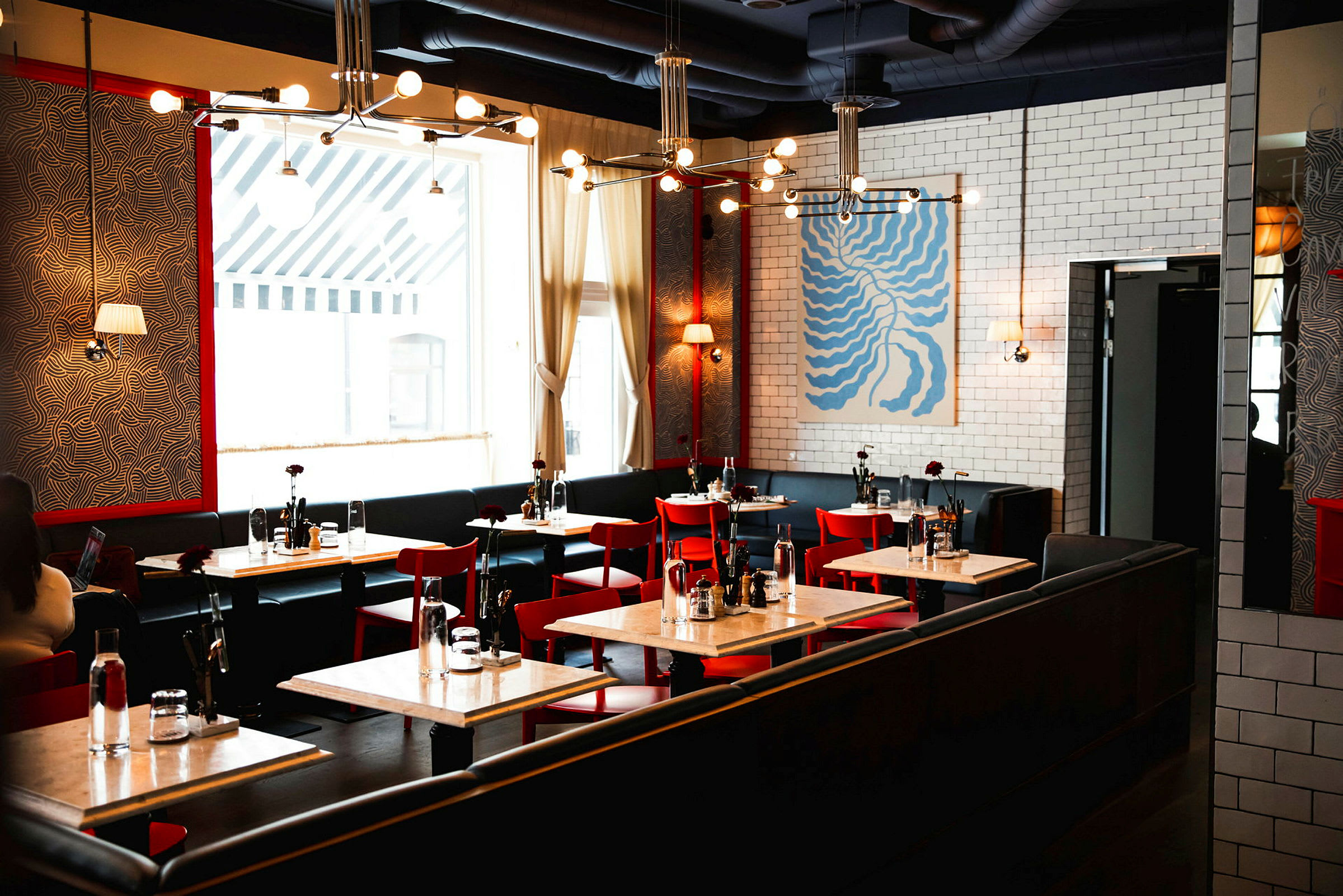 En moderne restaurant med røde stoler, hvite bord og vegger dekorert med kunst og mønstre. (AI-generert tekst)