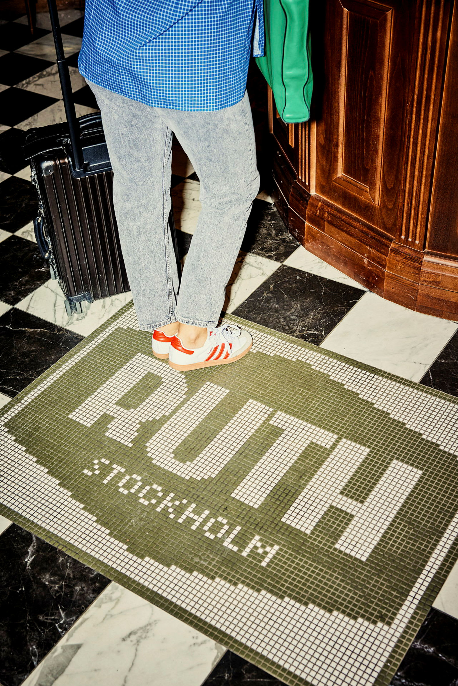 Person står med koffert på en gulvmosaikk som har teksten 'RUTH Stockholm'. (AI-generert tekst)