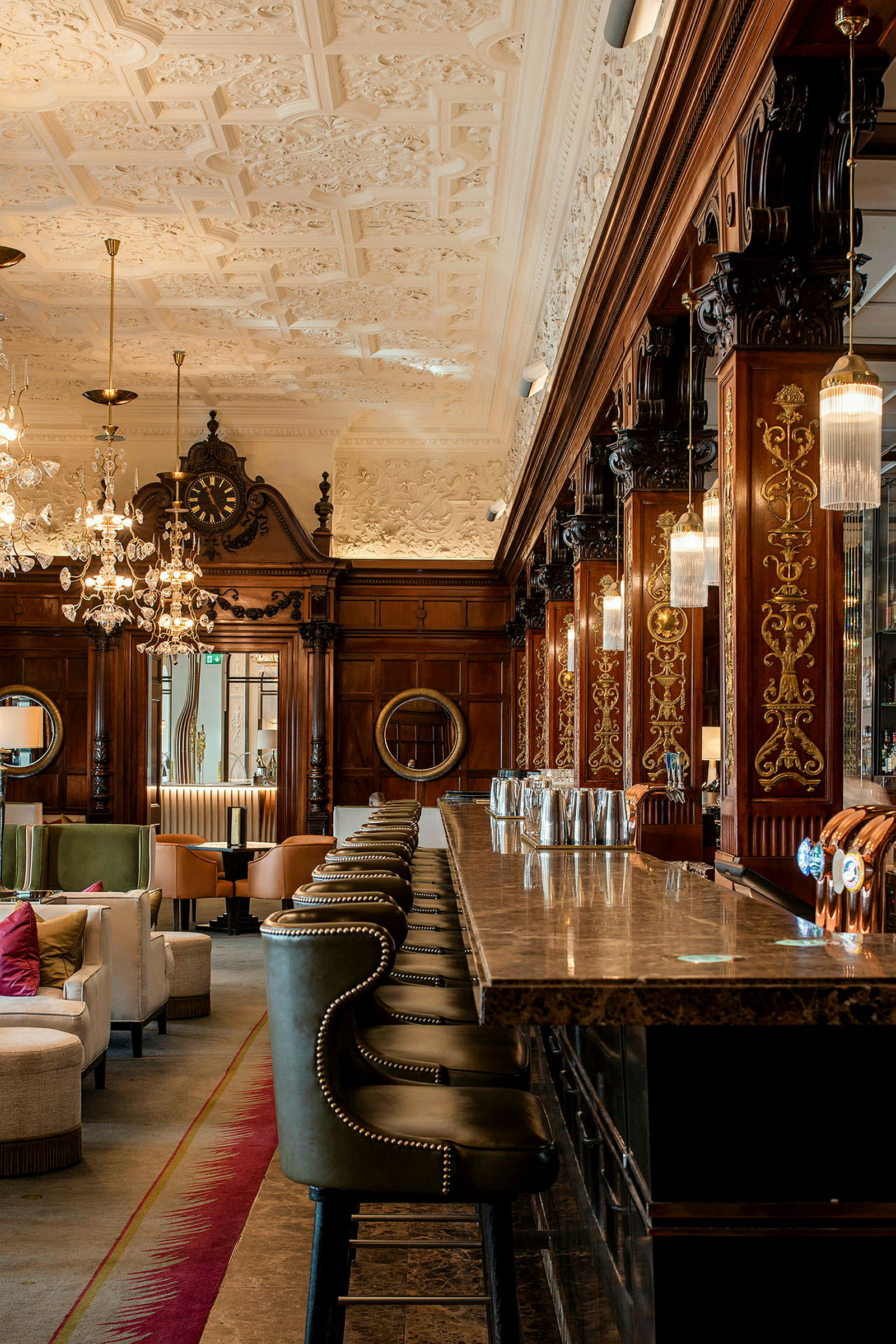 Elegant hotellbar med marmordisk og komfortable sitteplasser, krystallkroner og utsmykket trepanel på veggene. (AI-generert tekst)