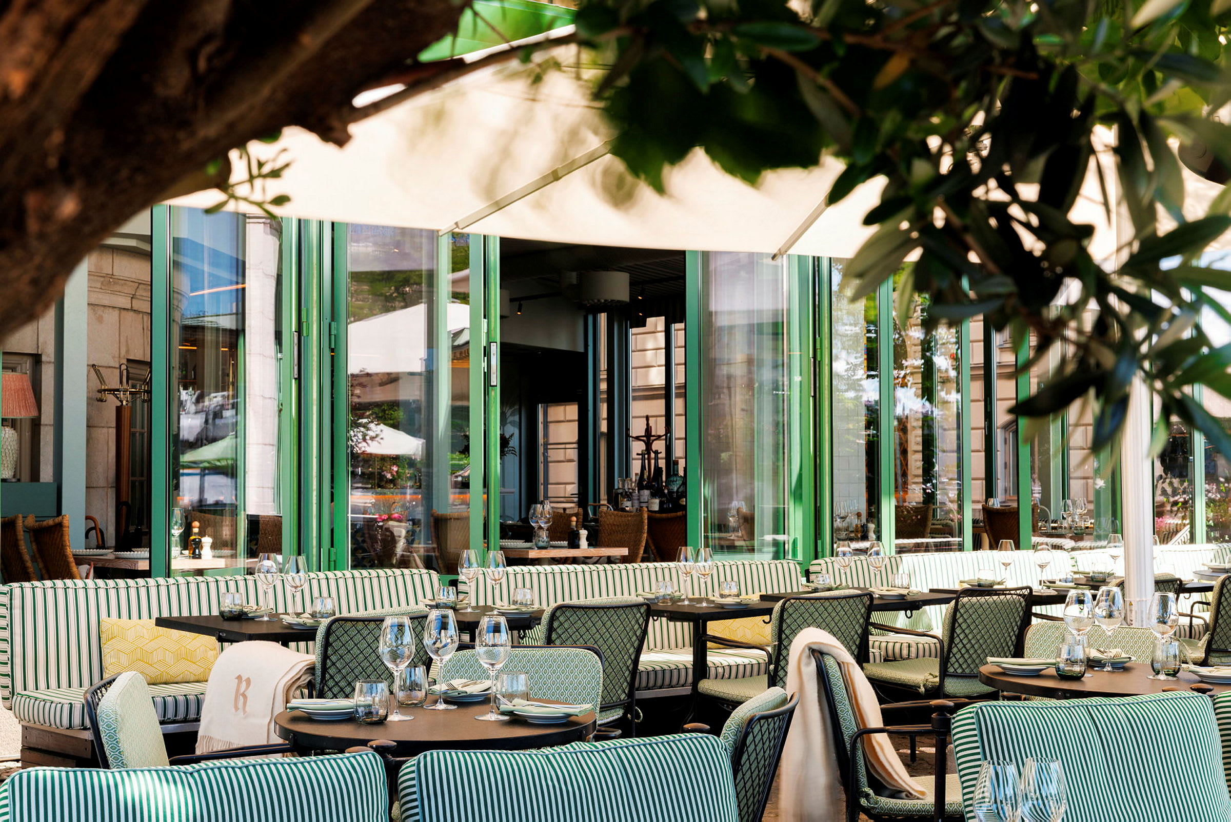 Restaurant med uteservering, flere bord og stoler samt stripete sitteputer. (AI-generert tekst)