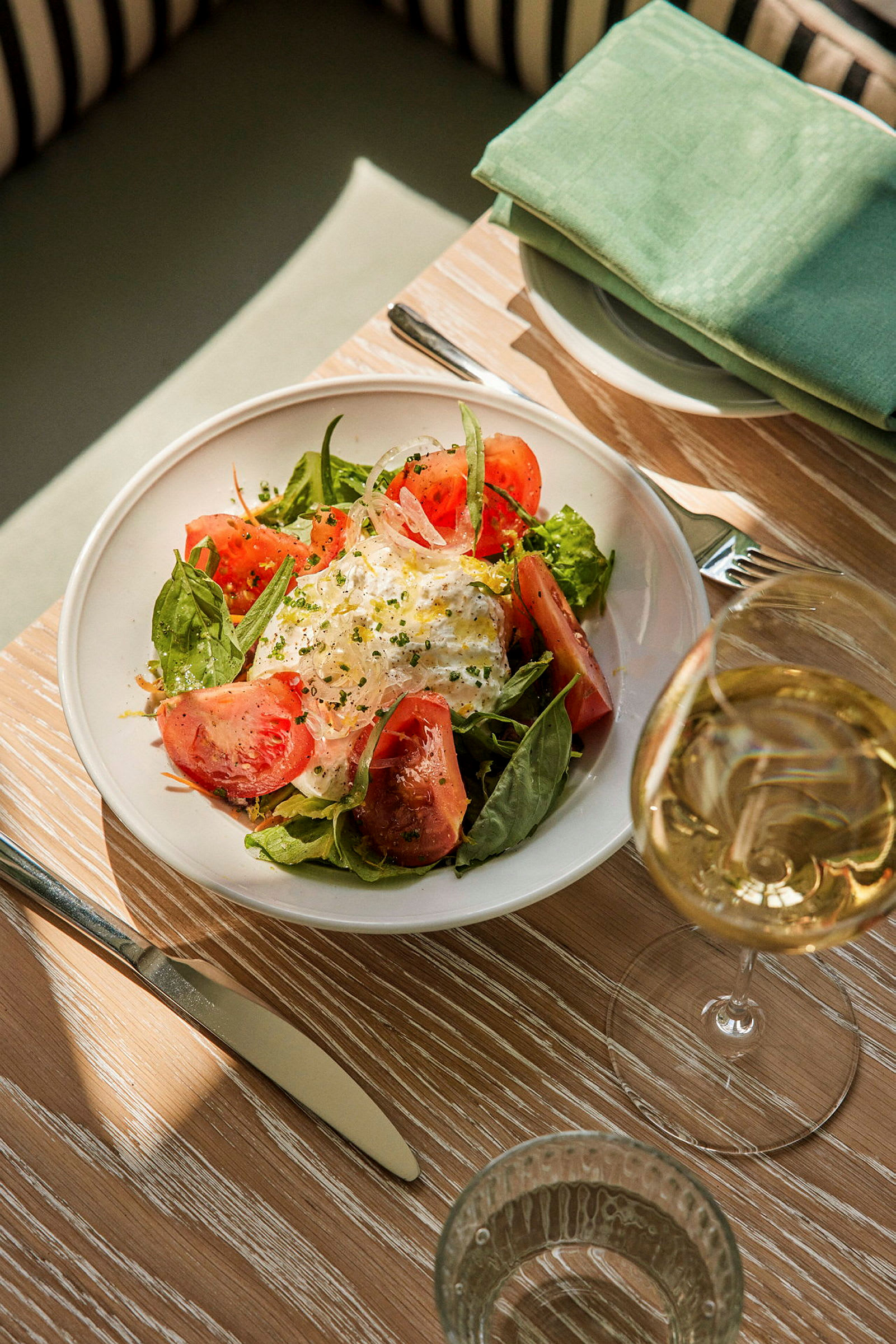 En tallerken med salat, tomat og burrata står på et bord ved siden av et glass vin. (AI-generert tekst)