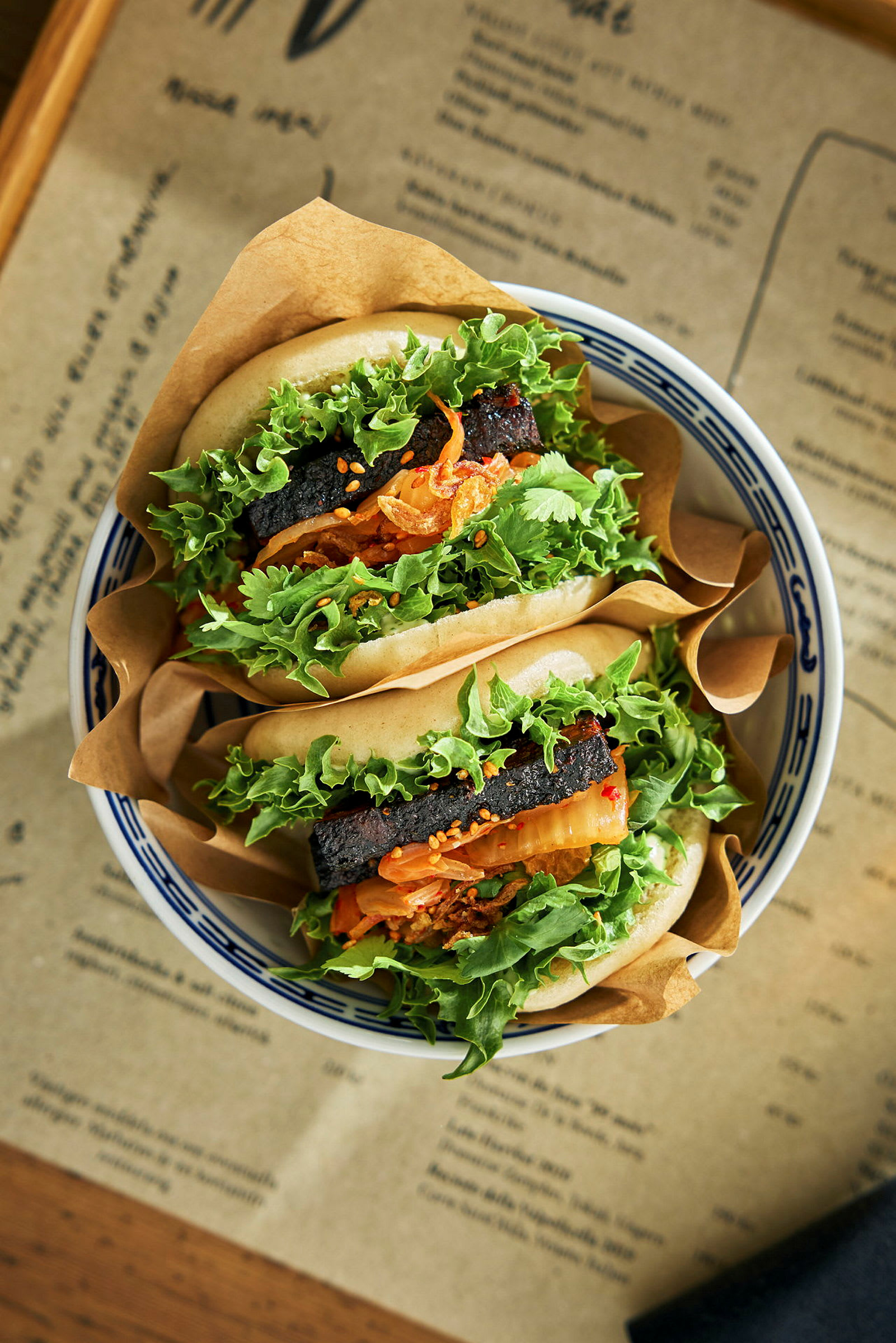 To bao boller fylt med grønn salat, kjøtt og andre ingredienser, servert i en skål. (AI-generert tekst)