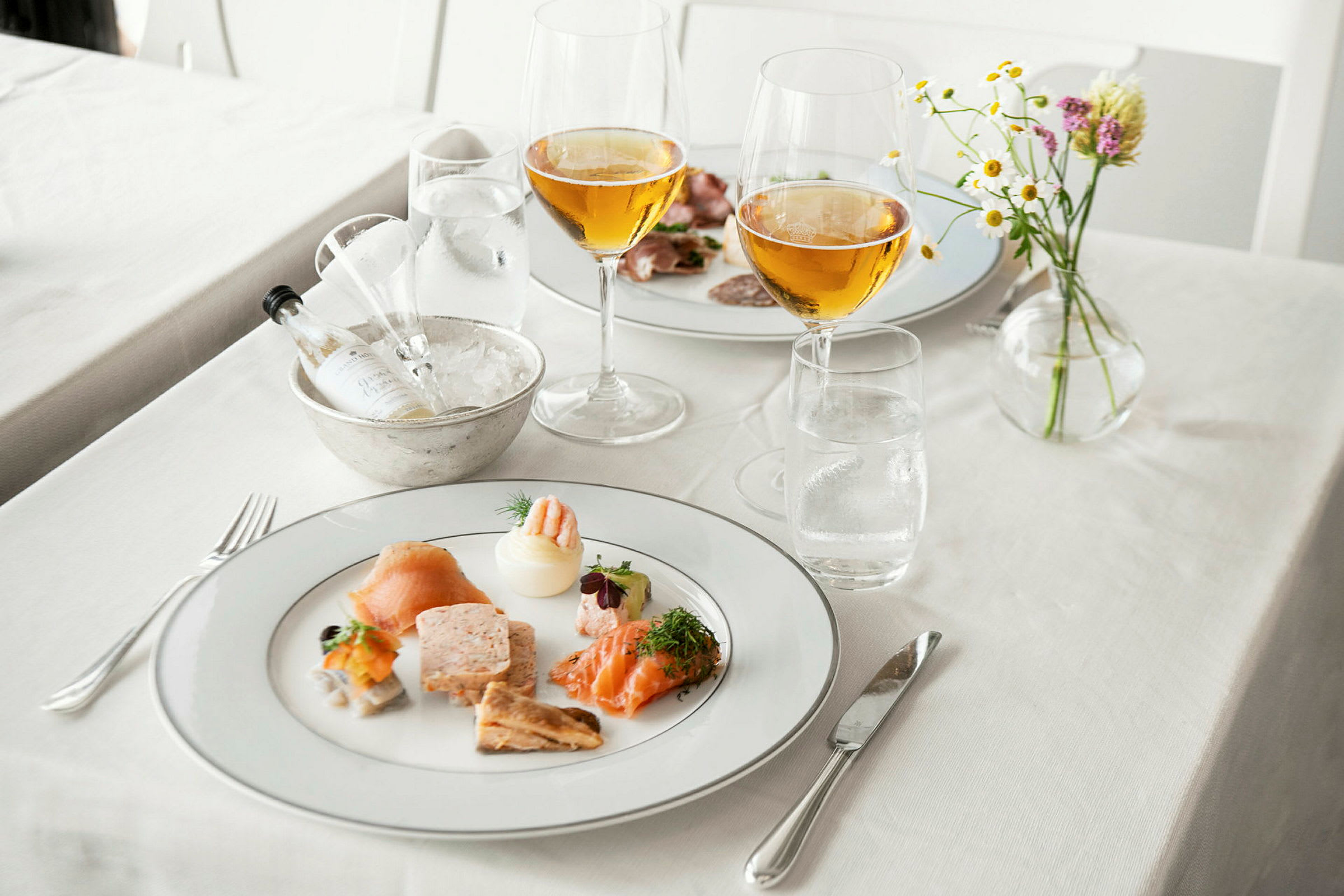 En tallerken med forretter, to glass drikke og en liten blomsterpotte på et dekket bord. (AI-generert tekst)