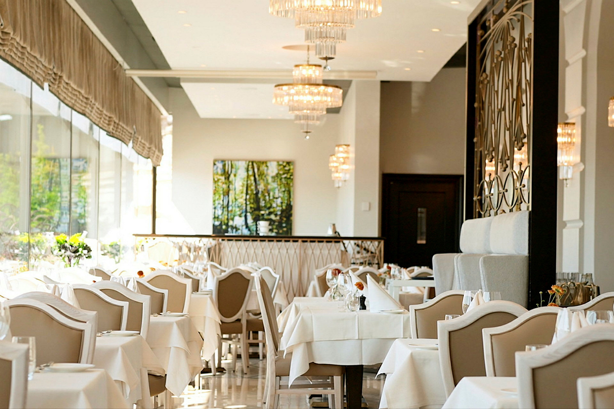En elegant restaurant med hvite duker, stoler med lyse ryggstøtter og lysekroner i taket. (AI-generert tekst)