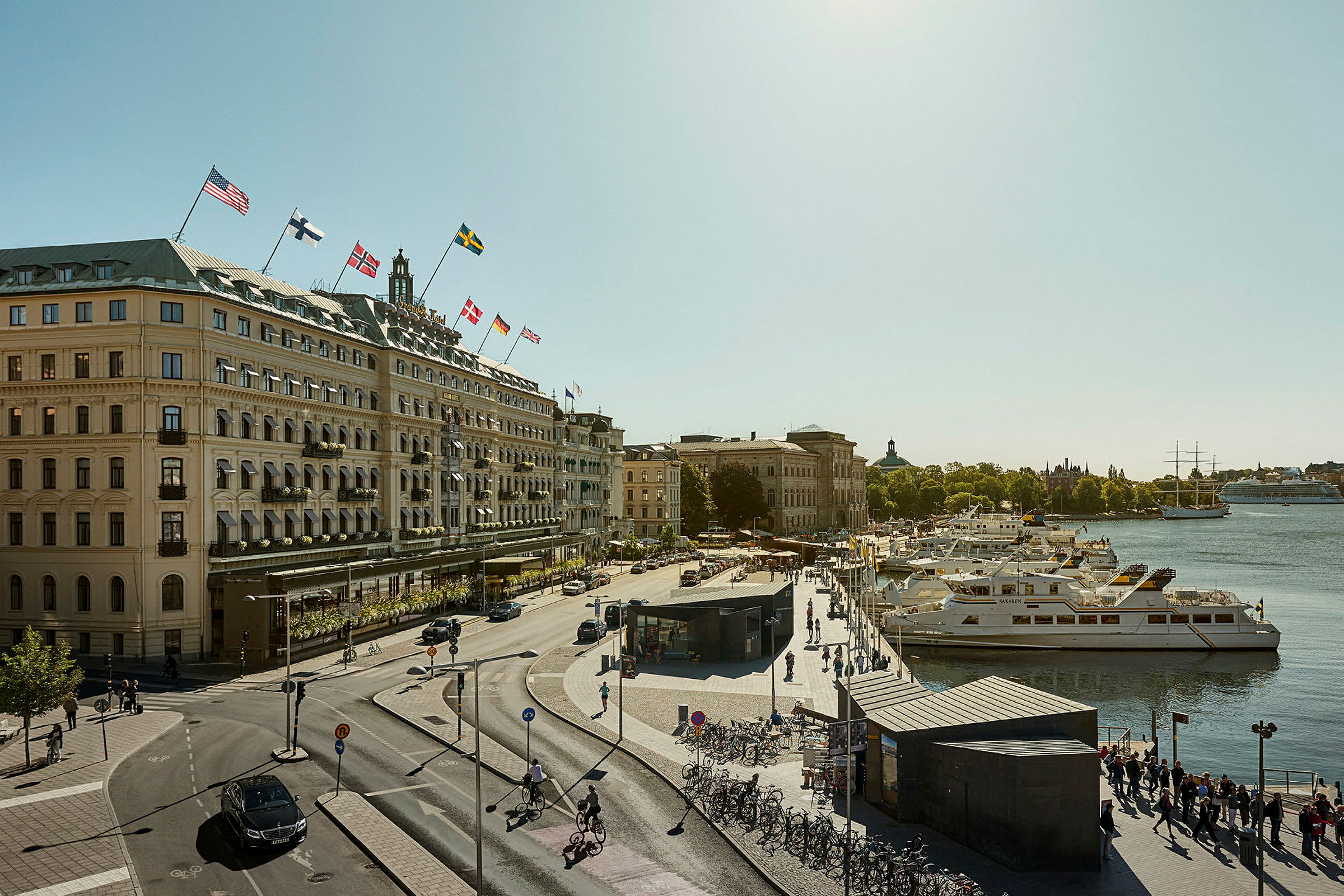 Utsikt over en by med en gate, bygninger med flagg og båter ved en brygge. (AI-generert tekst)