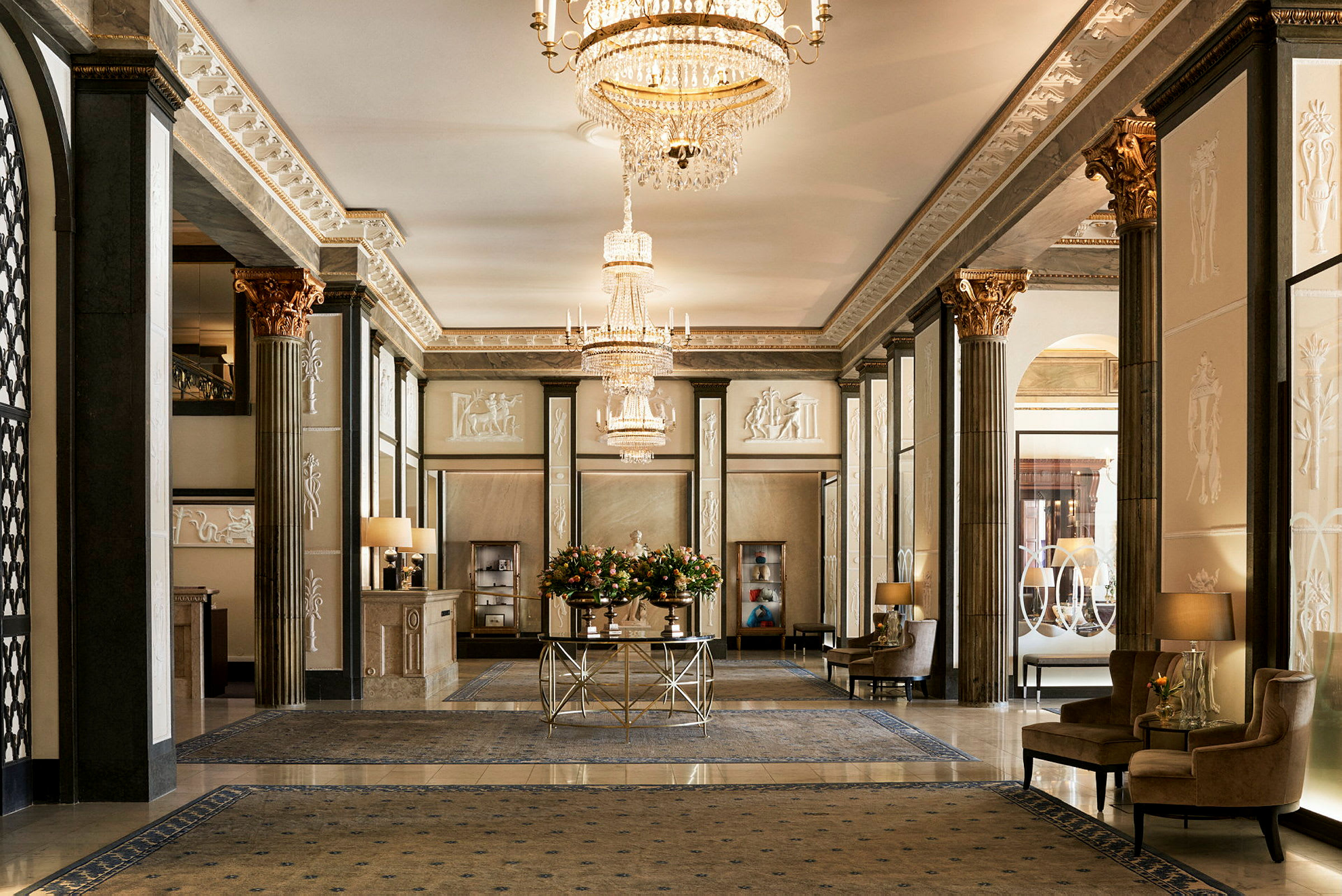 En elegant hotellobby med lysekroner, forgylte detaljer og komfortable sittemøbler. (AI-generert tekst)
