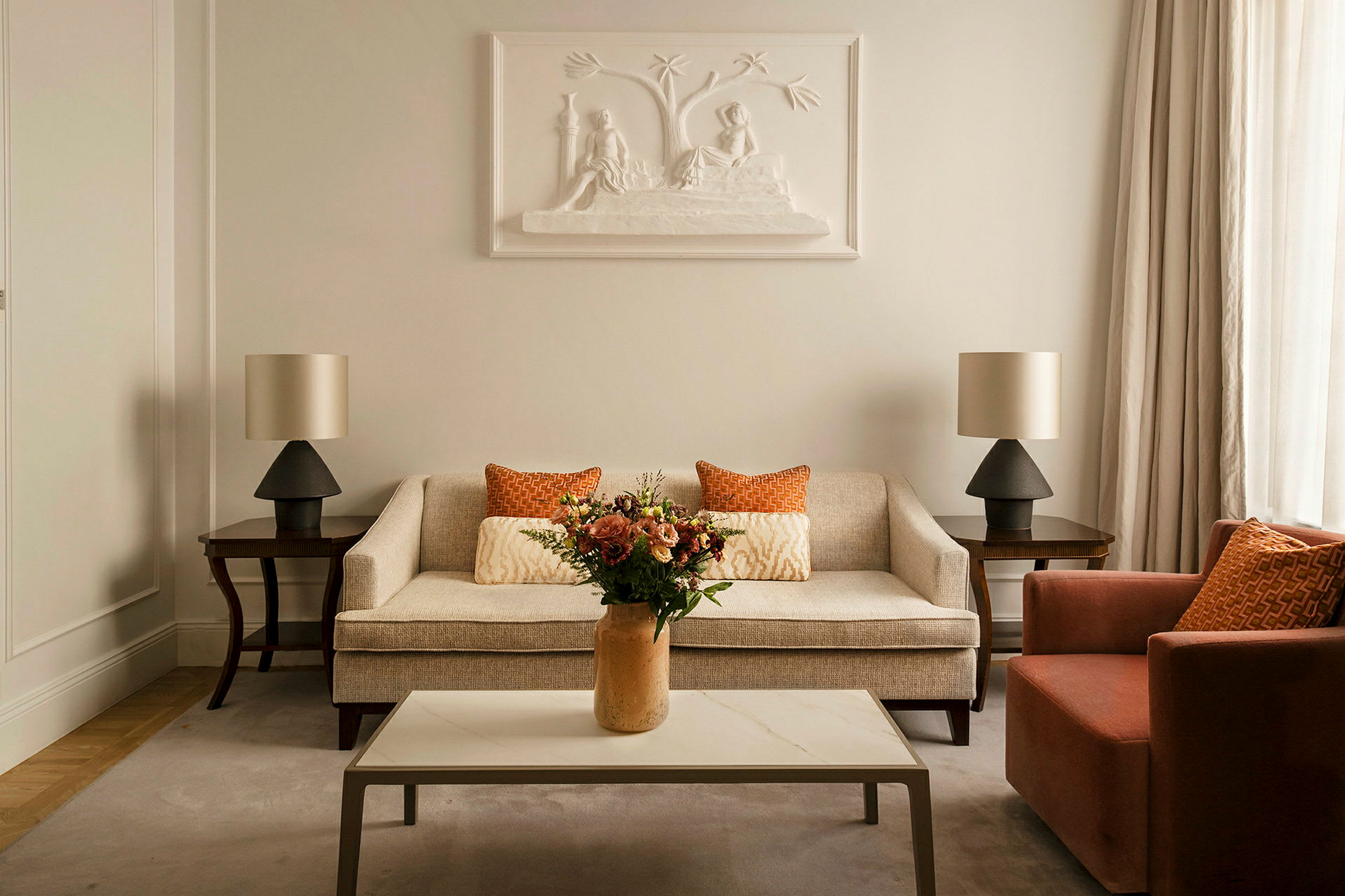 En stue med sofa og lenestol, samt et sofabord med en vase fylt med blomster. (AI-generert tekst)
